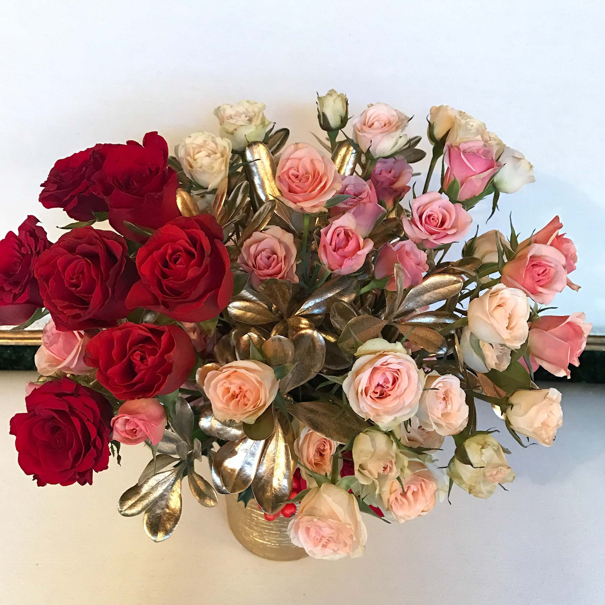 Bouquet of red and blush roses in a gold vase with metallic leaves