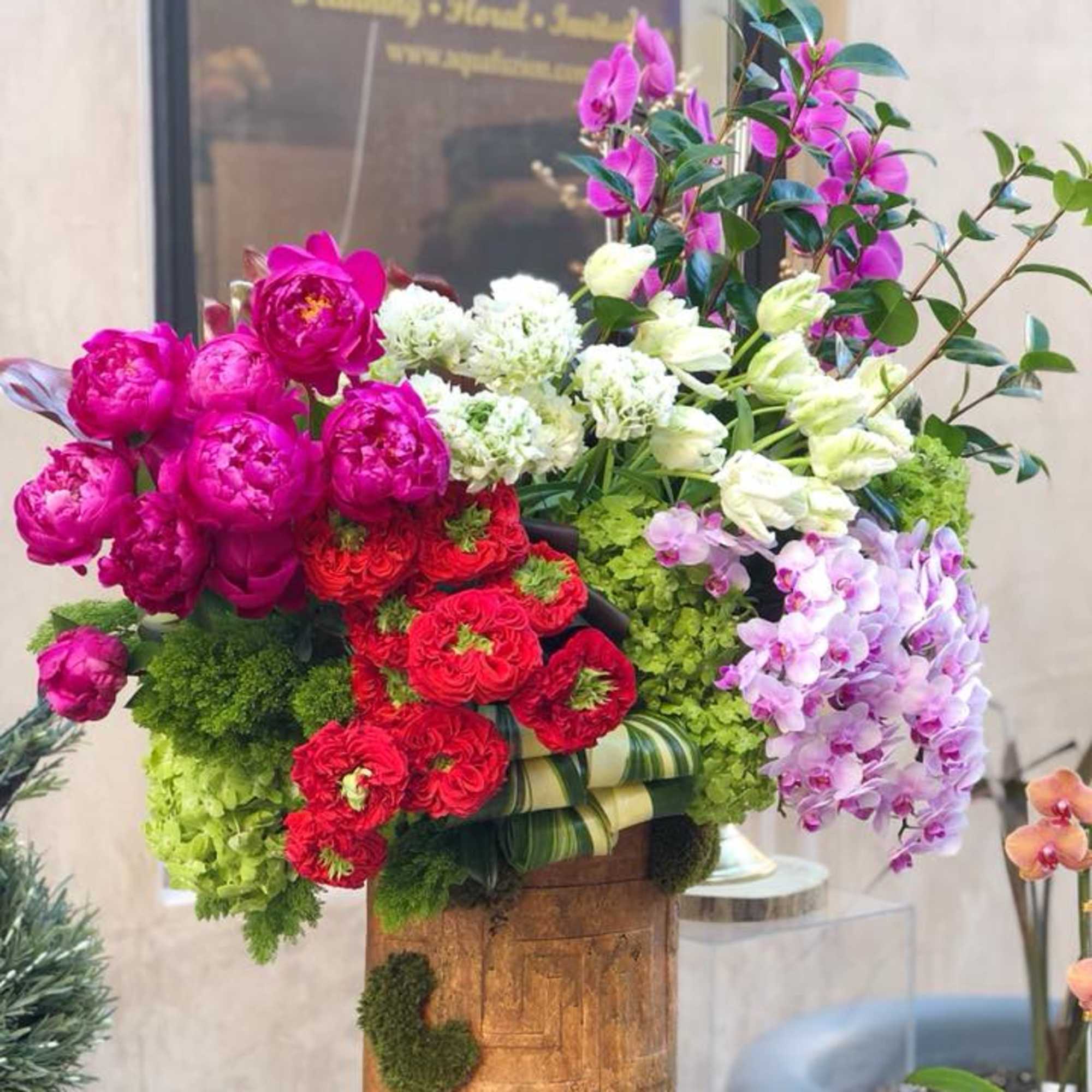 Colorful floral arrangement with peonies, roses, orchids, and hydrangeas in a wooden container