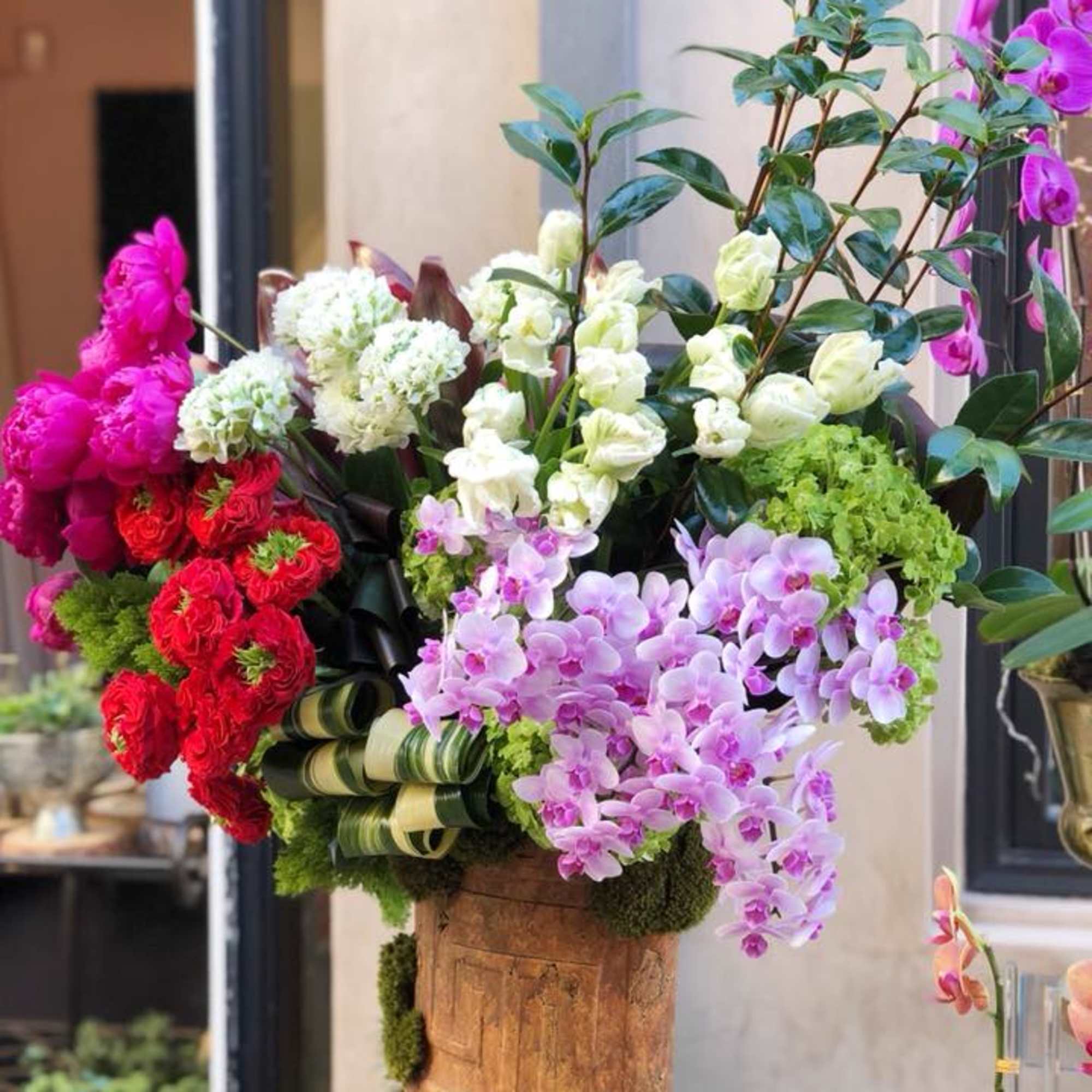 Tall floral arrangement with orchids, roses, and hydrangeas in a wooden container