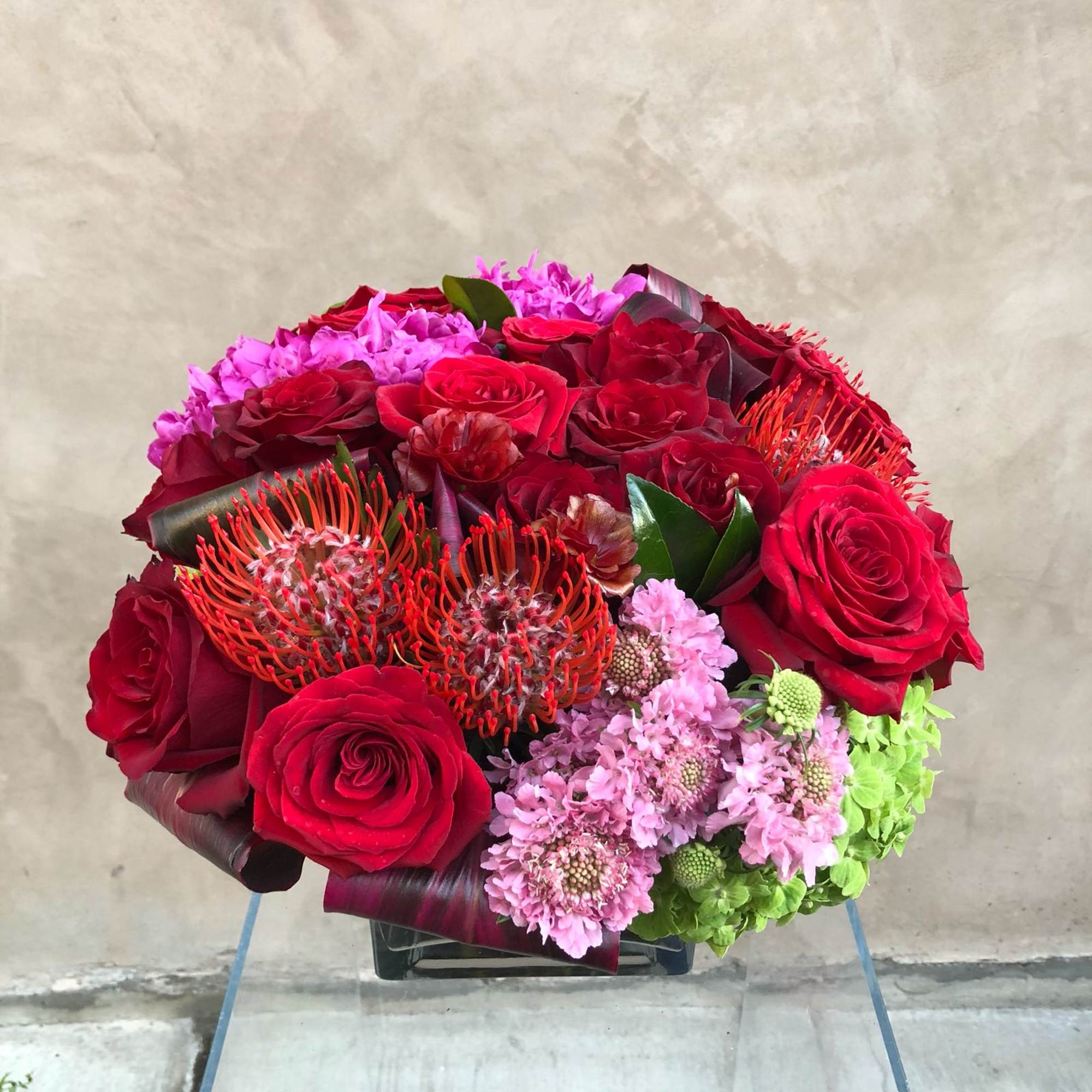 Red roses and pink flowers arranged in a low square vase