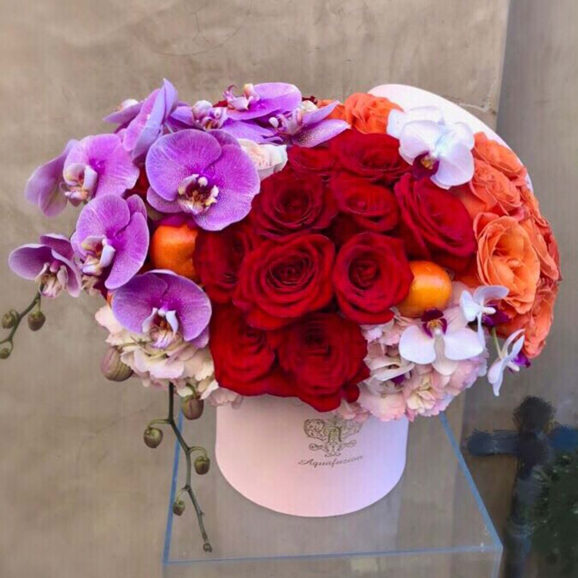 Round bouquet of red roses, purple orchids, and orange roses in a white hat box