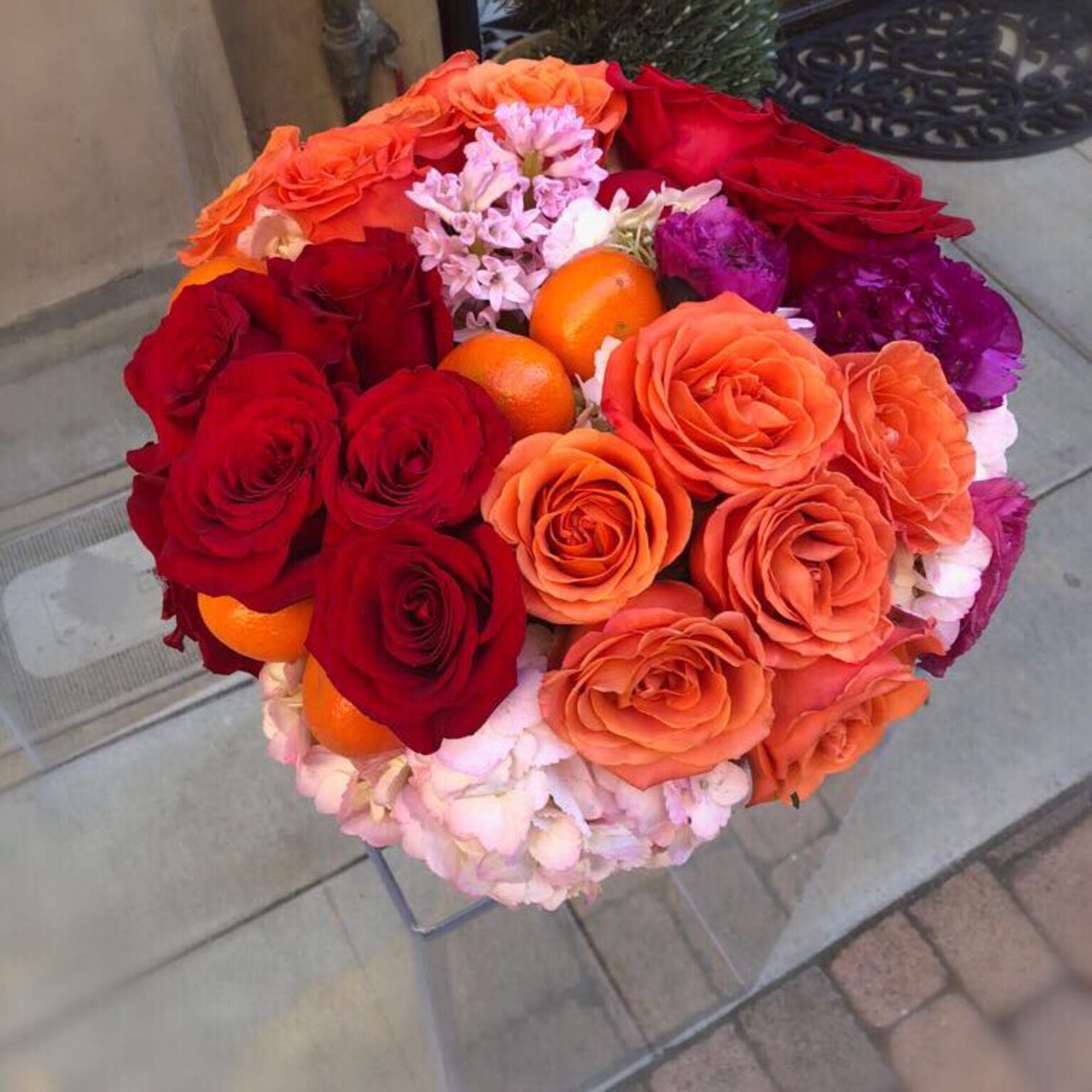 Round bouquet of red and orange roses with purple flowers and oranges
