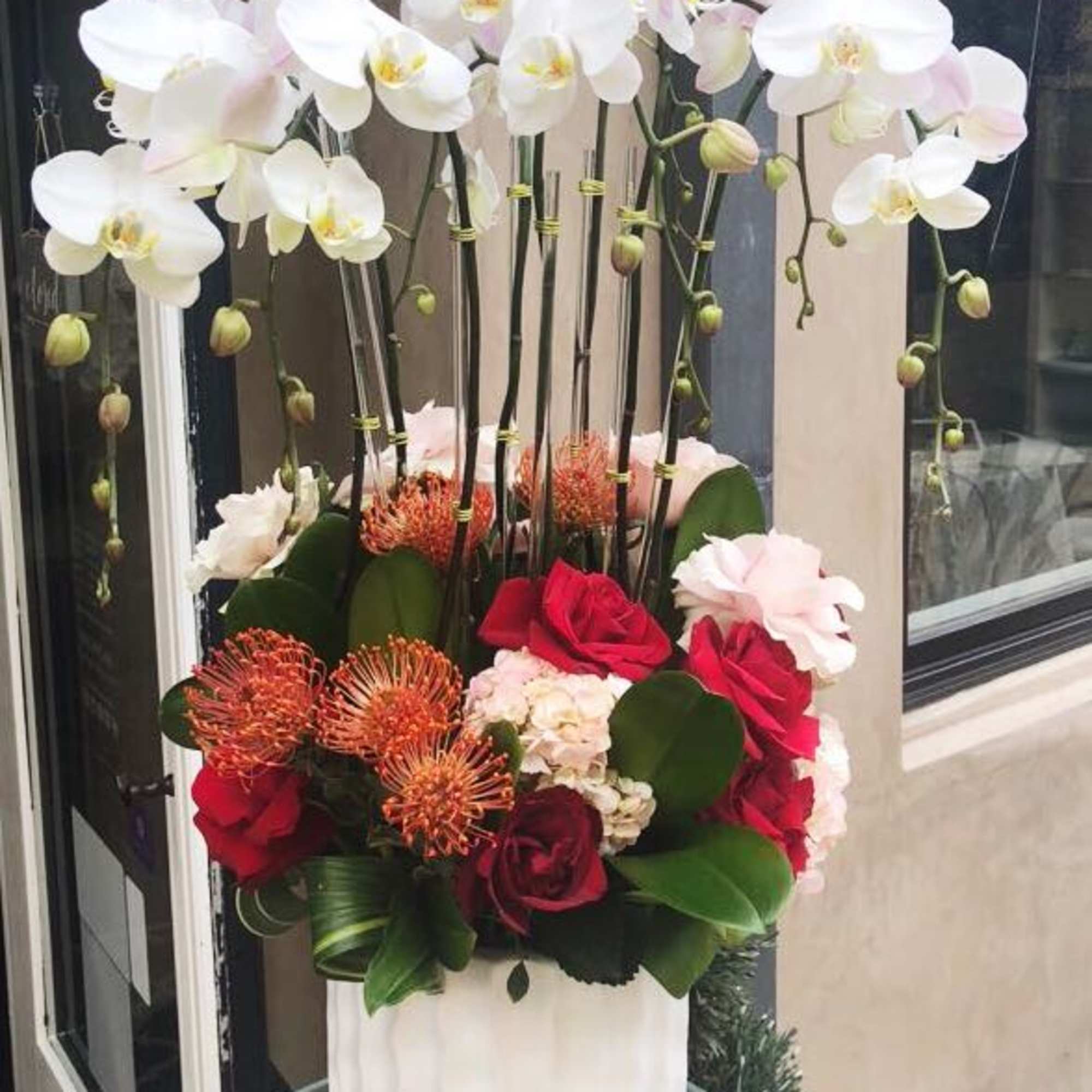 Tall floral arrangement with white orchids and red roses in a white vase