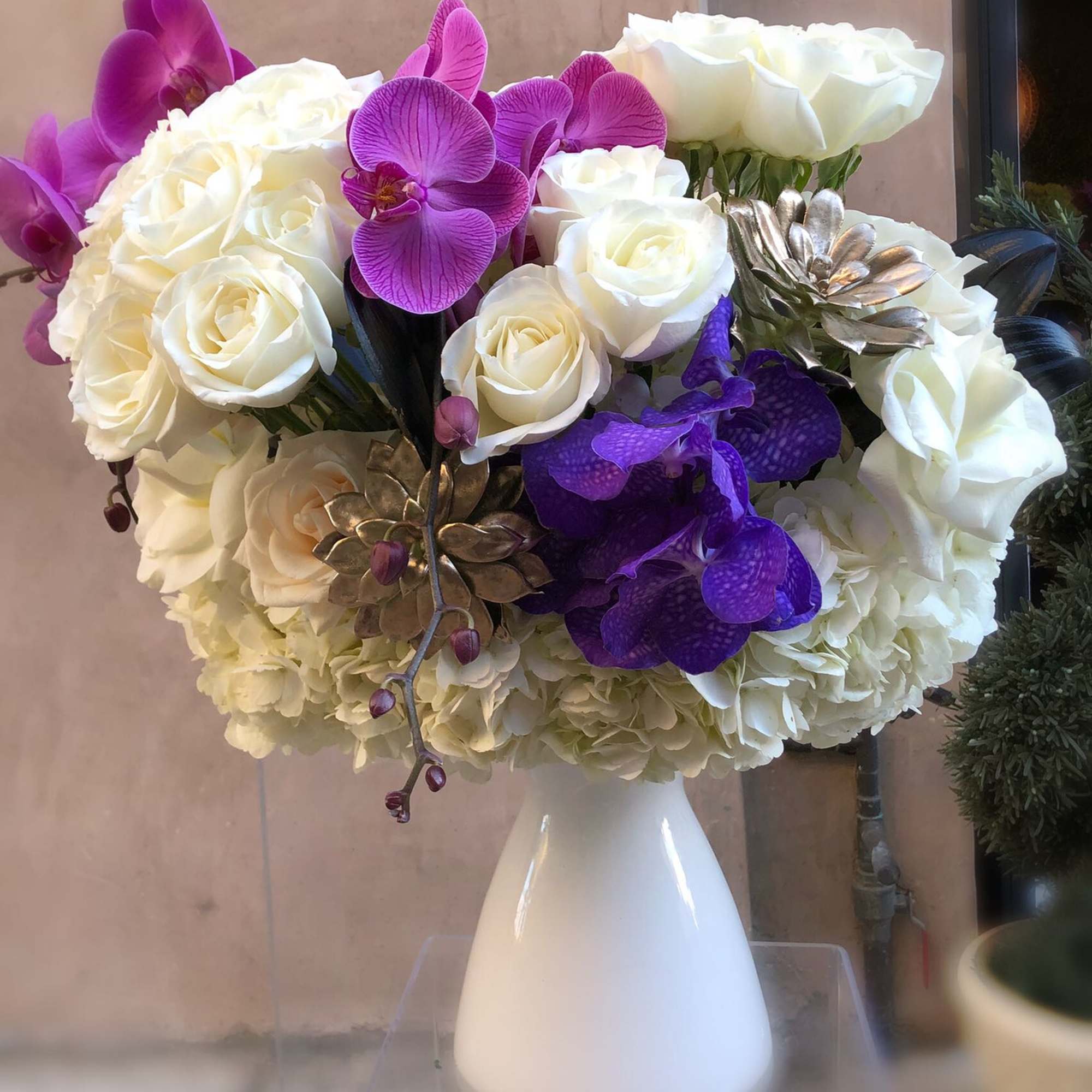 White roses and purple orchids arranged in a white vase