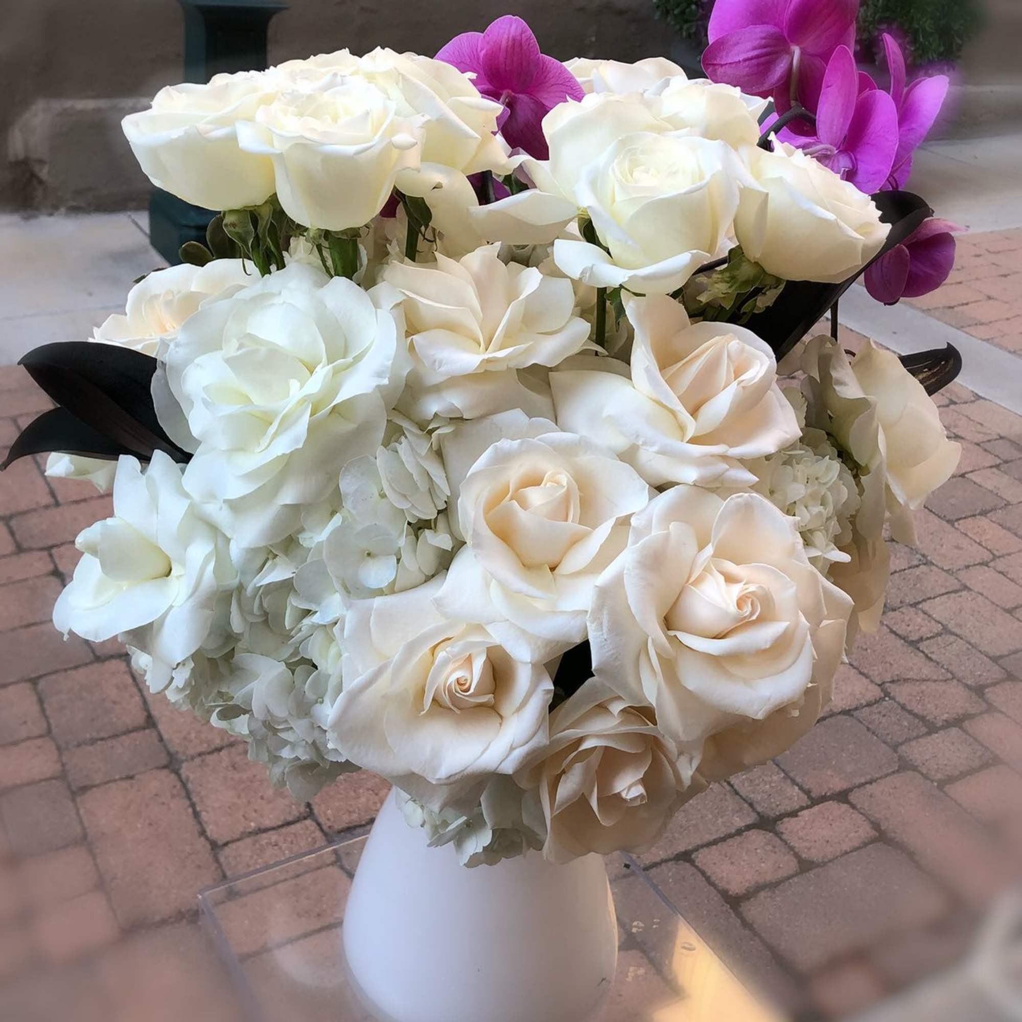 White roses and orchids arranged in a white vase