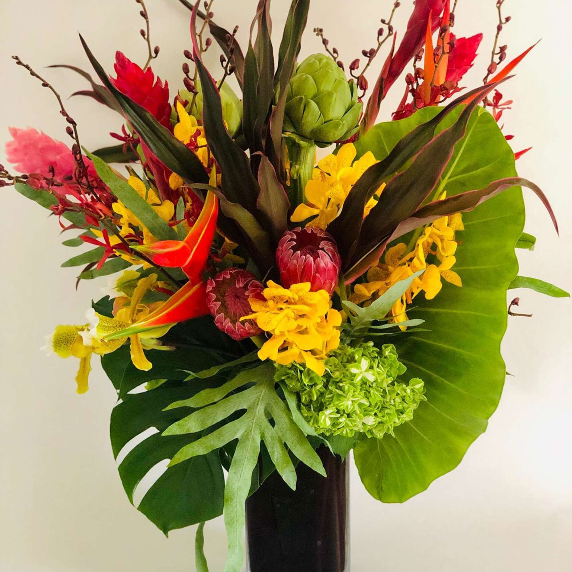 Tropical bouquet in a tall glass vase with red, yellow, and green blooms