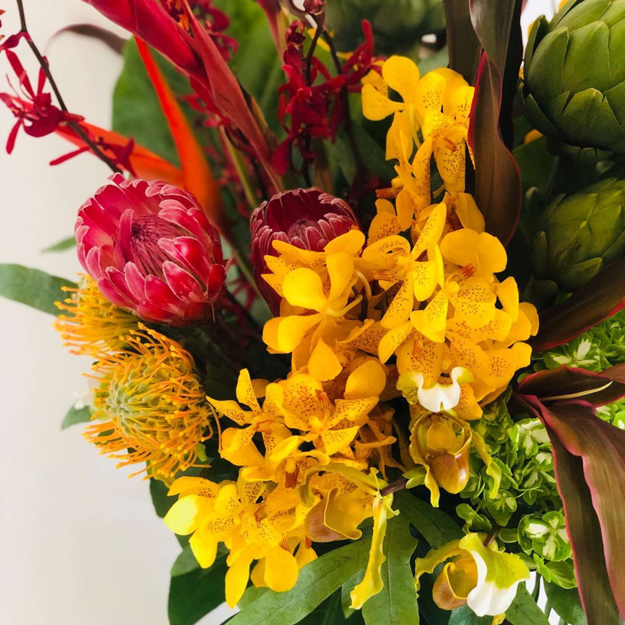 Tropical bouquet with yellow orchids, red protea, and green foliage