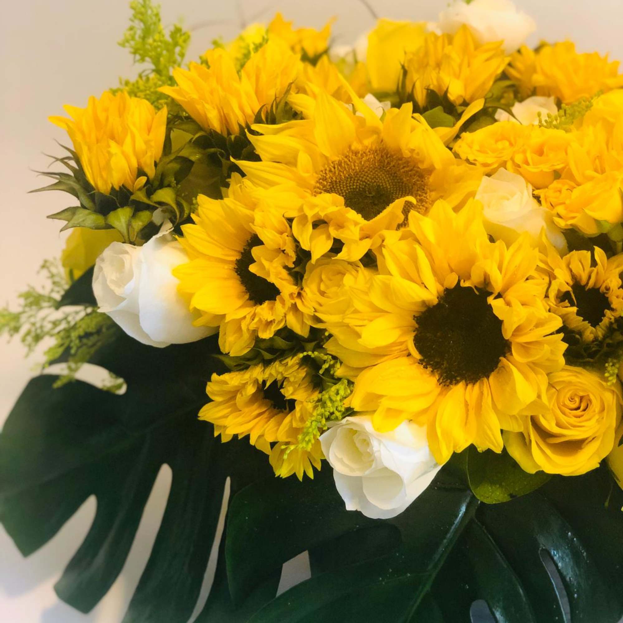 Yellow sunflower bouquet with white roses and large split leaves