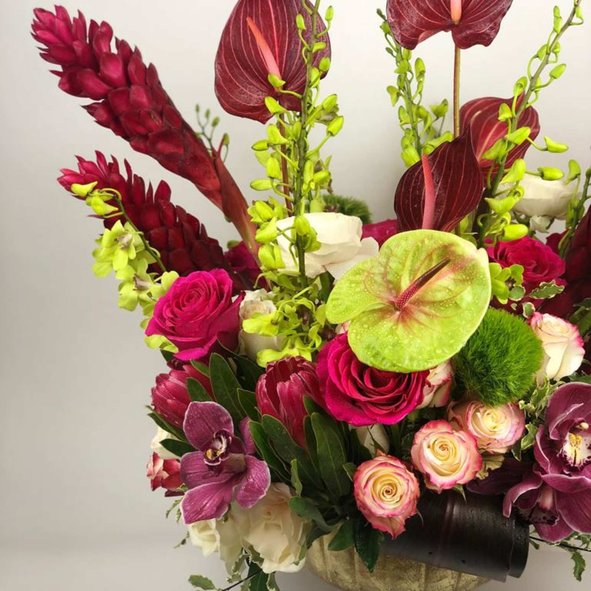 Tropical bouquet with burgundy anthuriums, pink roses, and lime-green accents in a gold vase