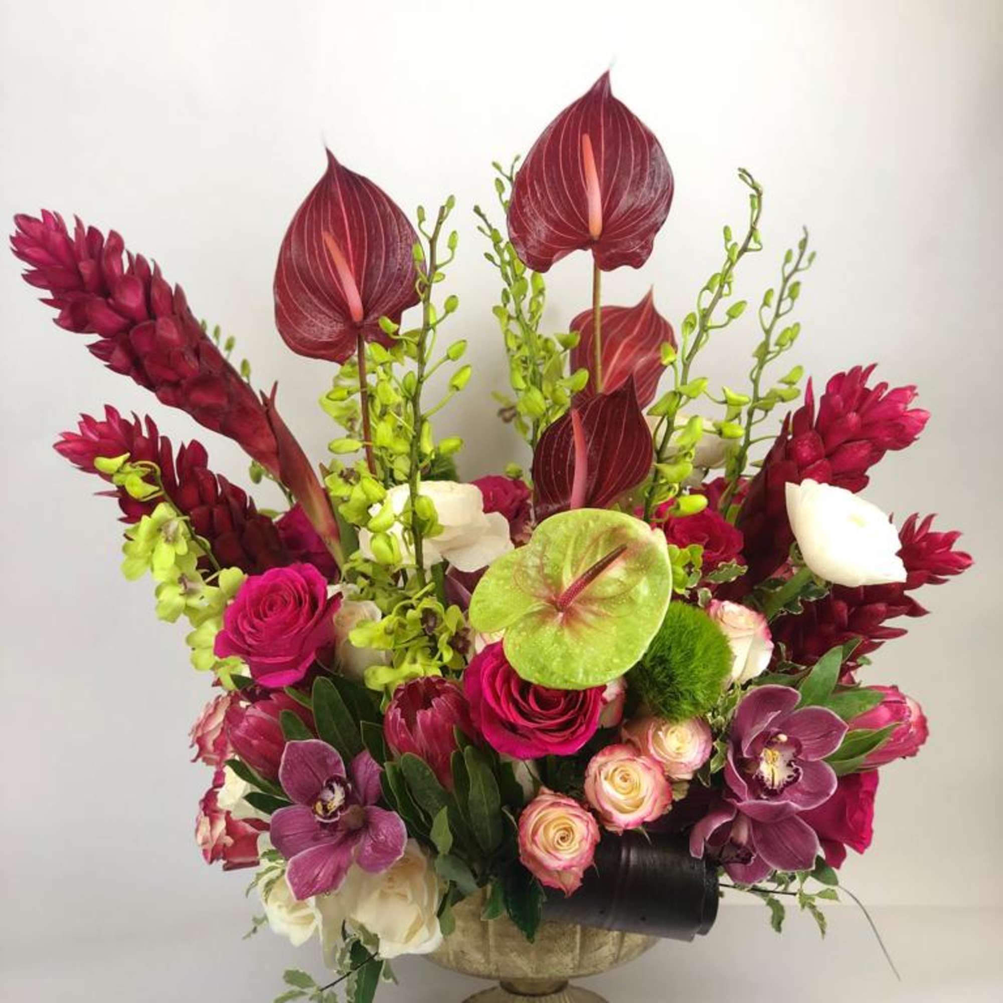 Tall arrangement of magenta and burgundy flowers in a pedestal vase