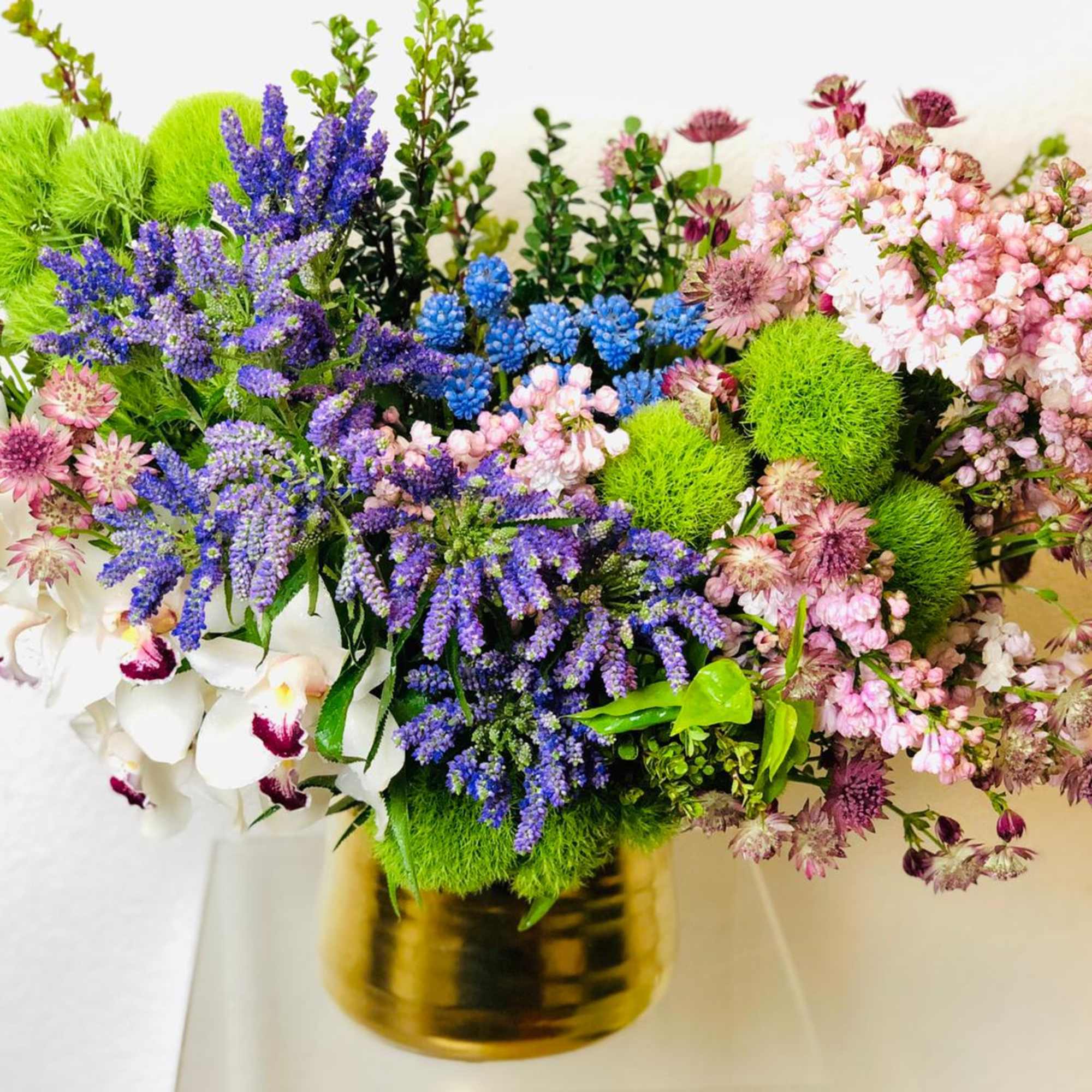 Mixed bouquet with purple, pink, white, and green flowers in a gold vase