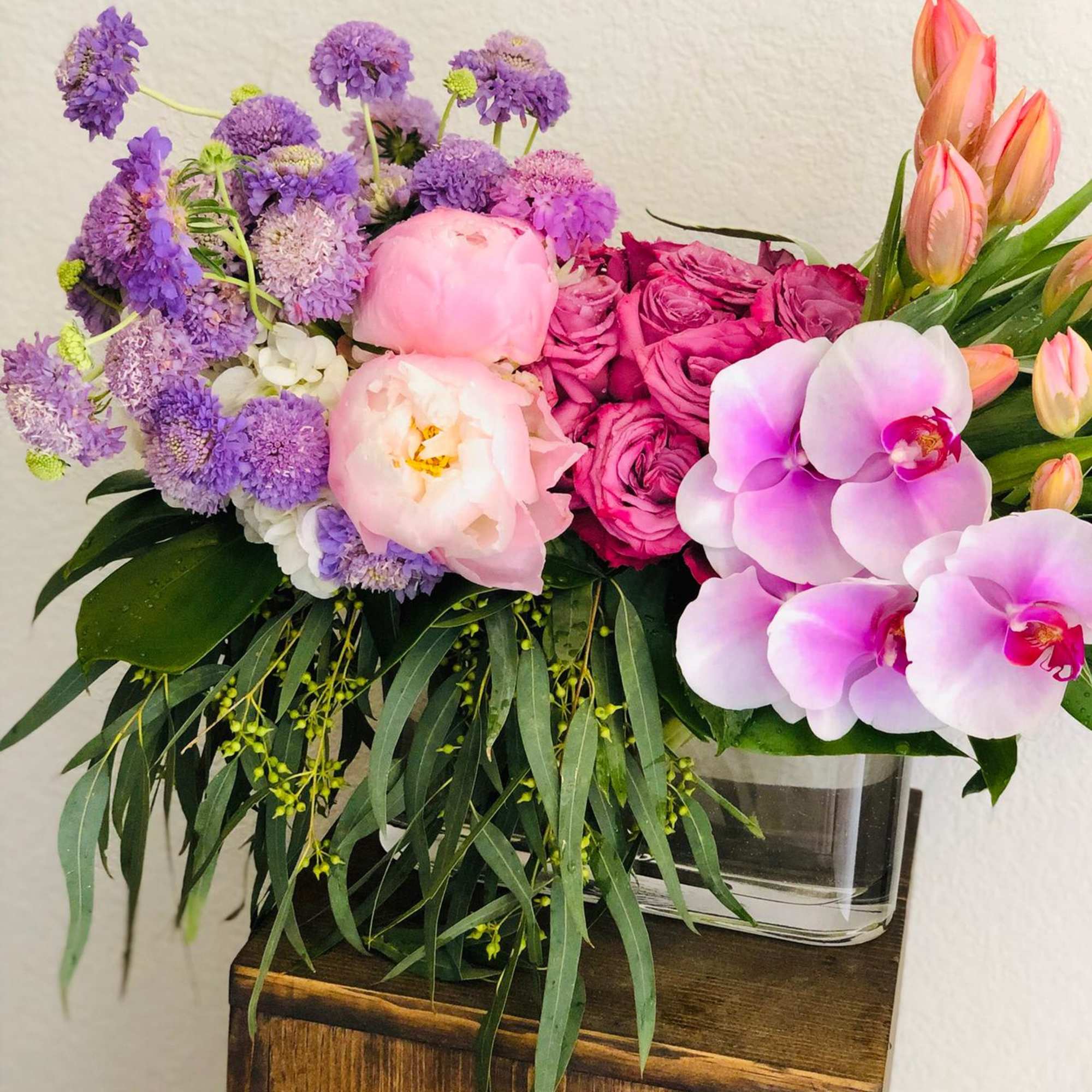 Mixed bouquet with purple blooms, pink roses, peonies, and orchids in a glass vase