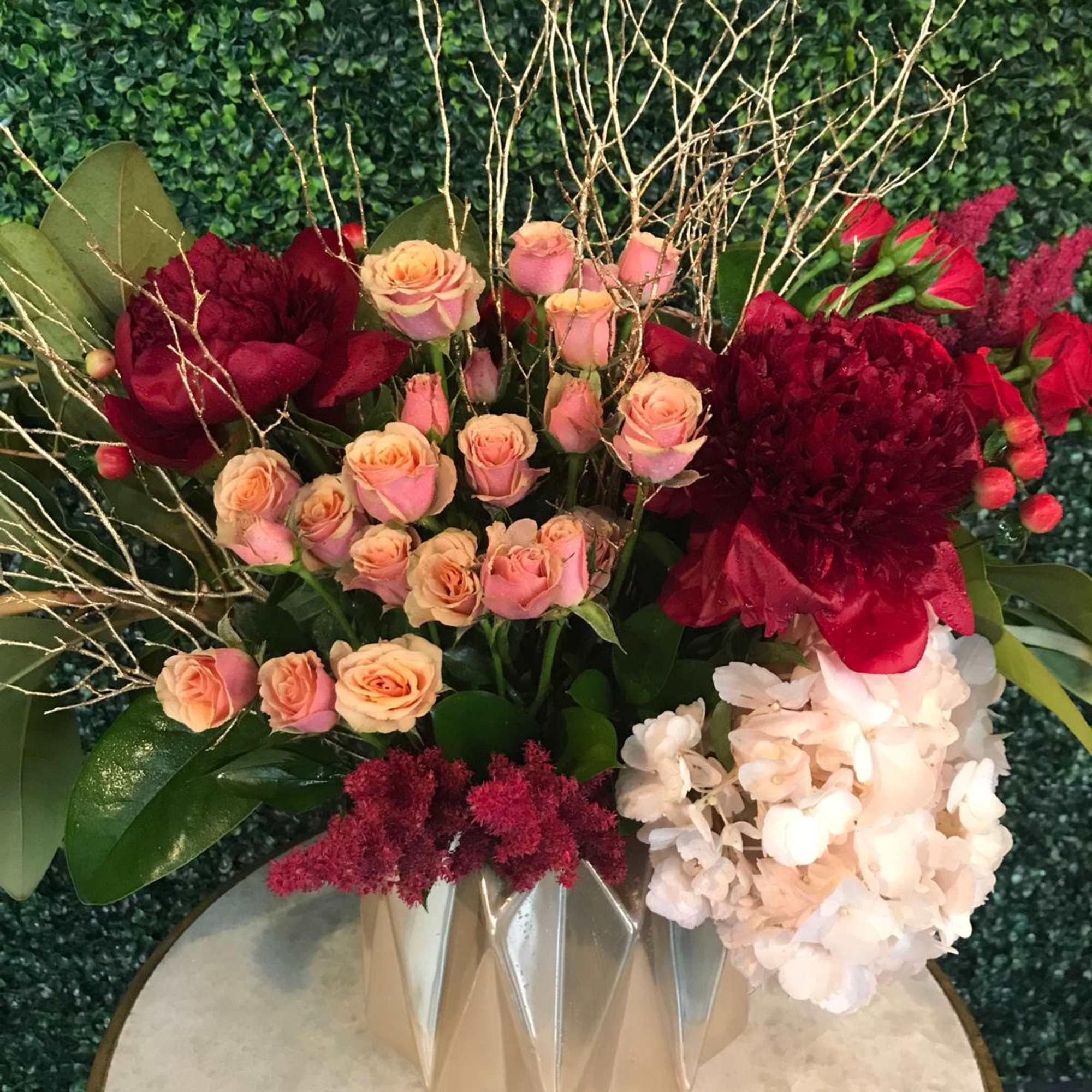 Mixed floral arrangement with pink roses, burgundy blooms, and white hydrangea in a geometric vase