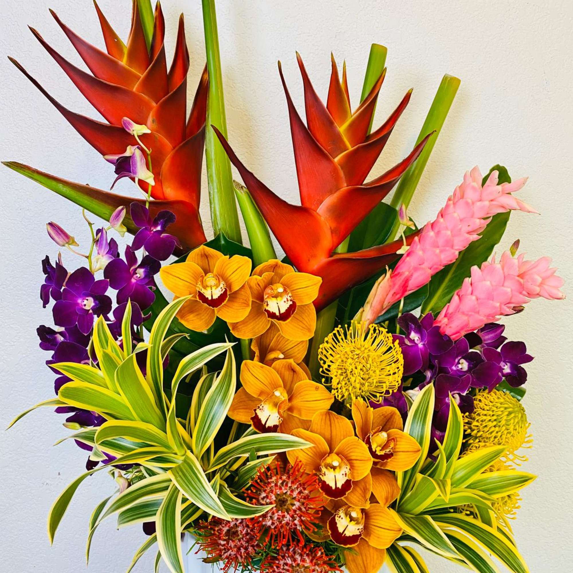Tropical arrangement with orange heliconia, orchids, and pink ginger in a white vase