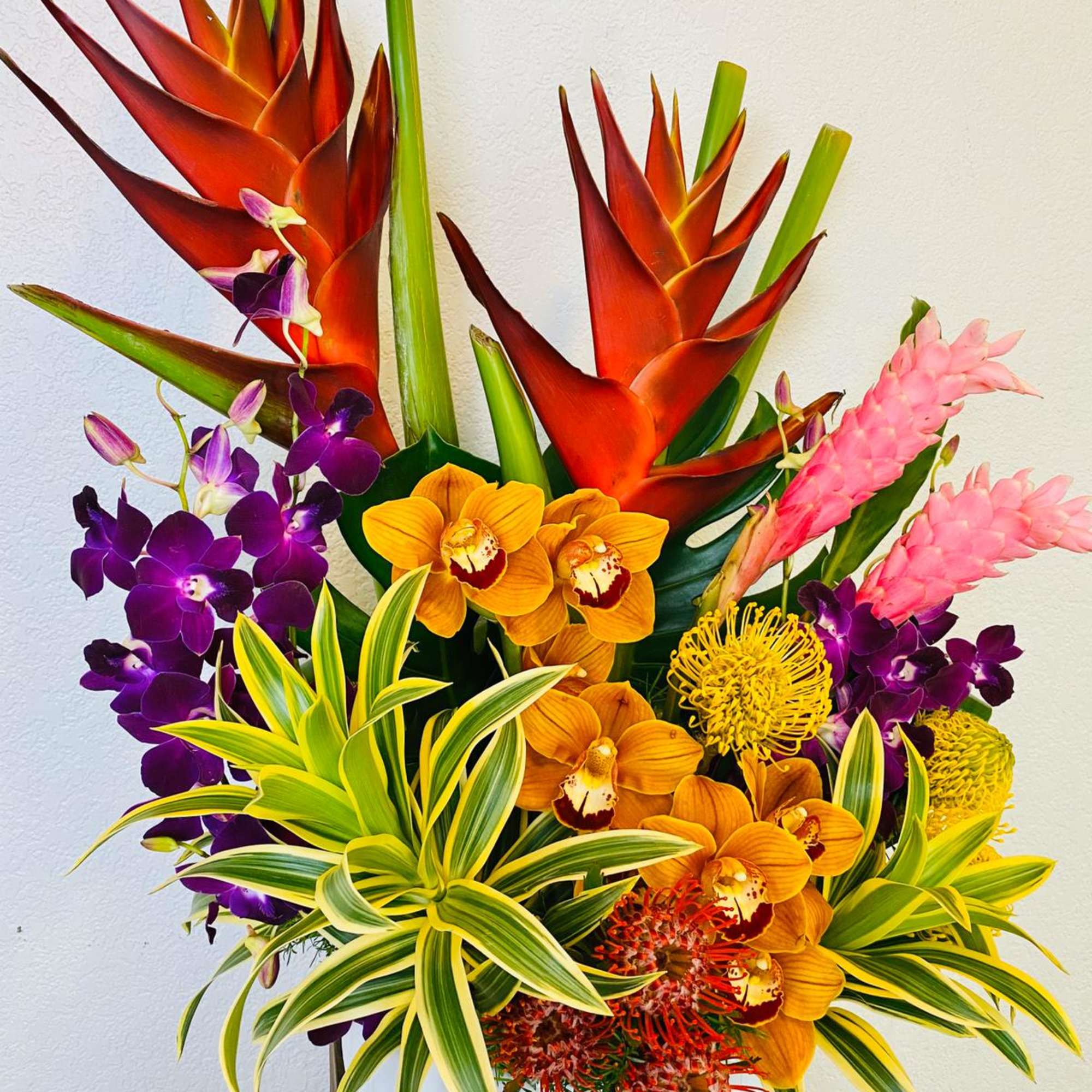 Tropical arrangement with orange heliconia, purple orchids, and pink ginger in a white vase