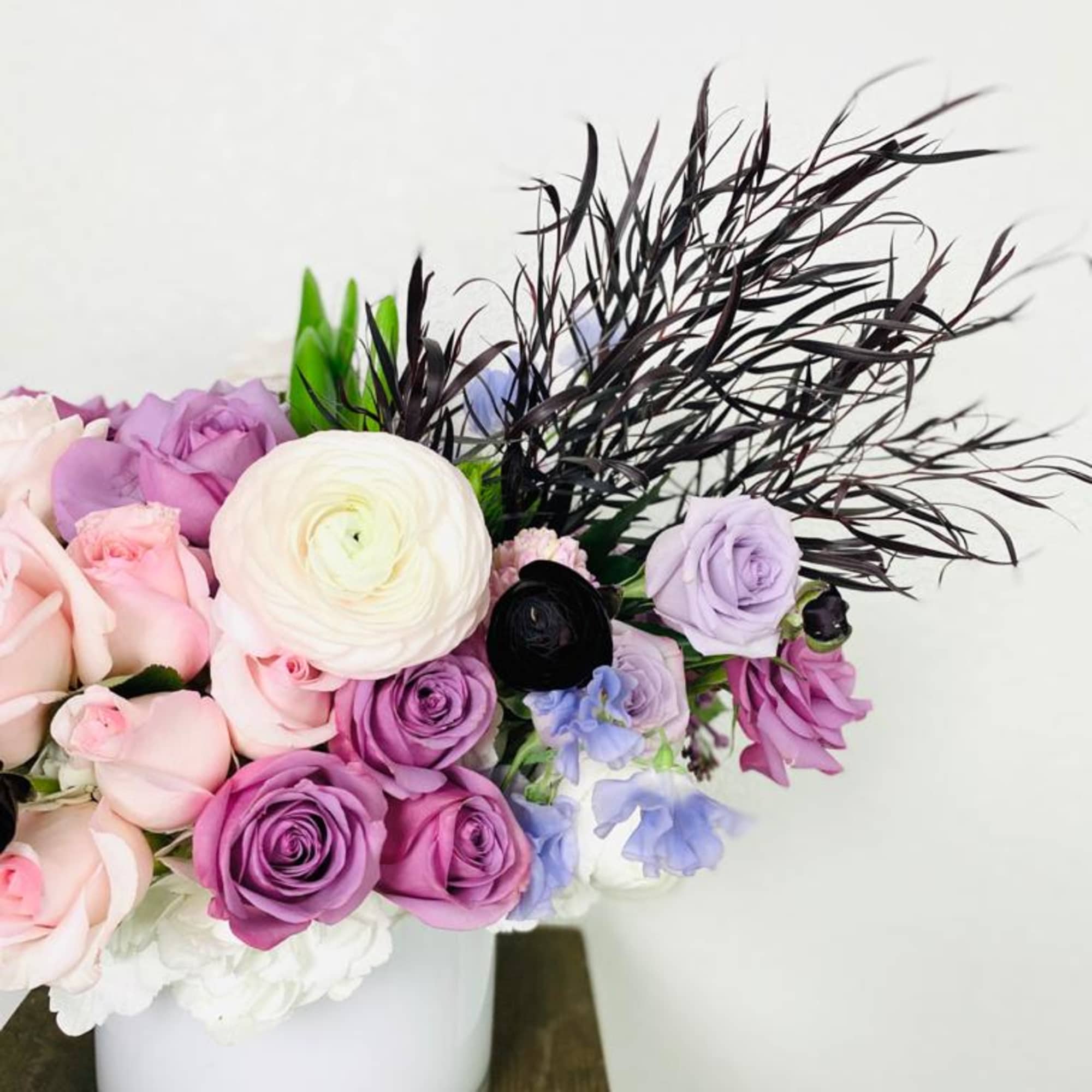Bouquet of pink and purple roses with white ranunculus in a white vase
