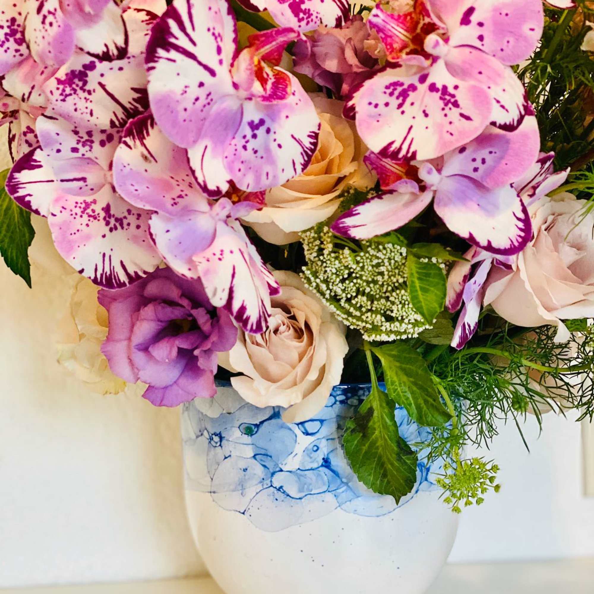 Bouquet of pink-and-white orchids and pale roses in a white vase
