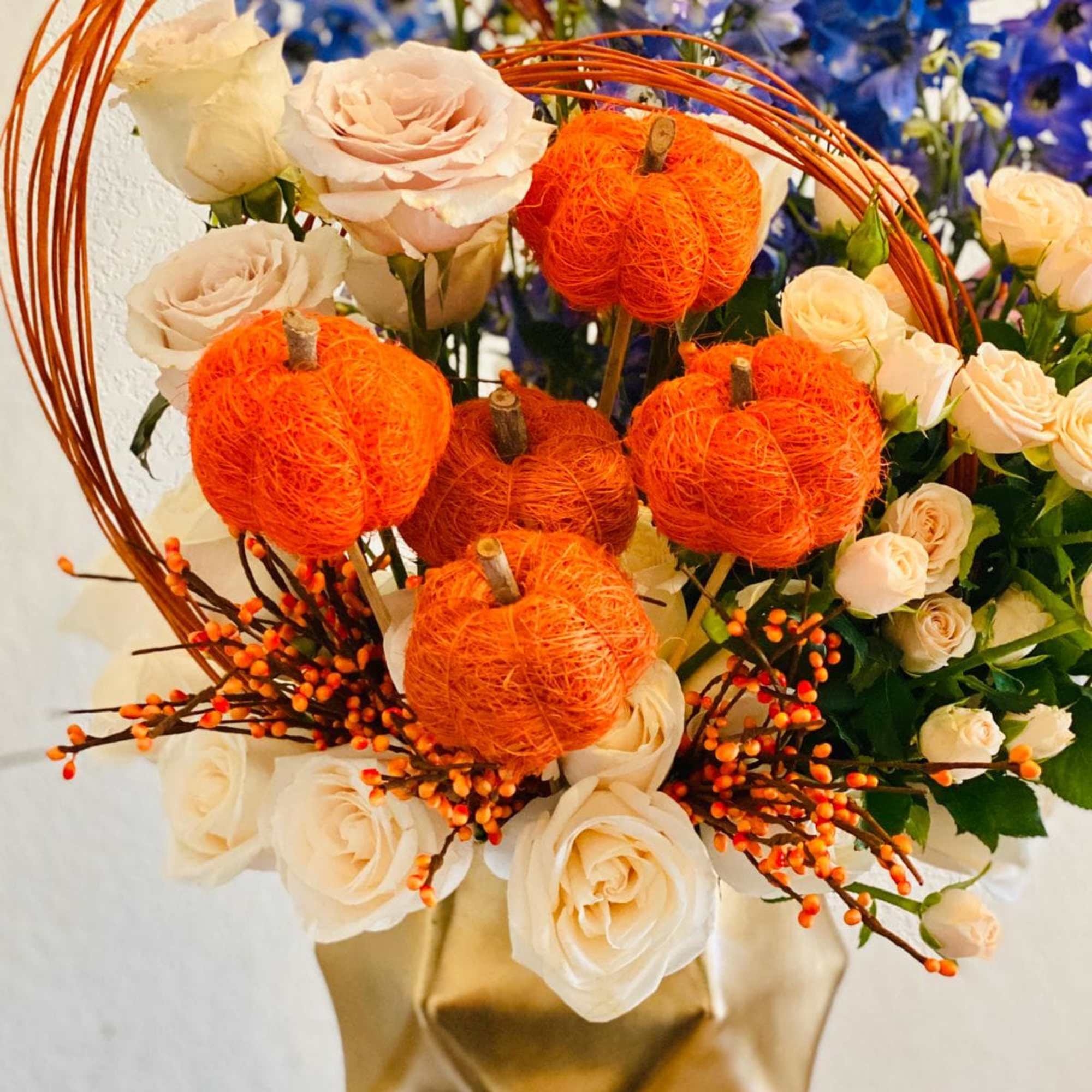 Cream roses with orange pumpkin accents in a gold vase