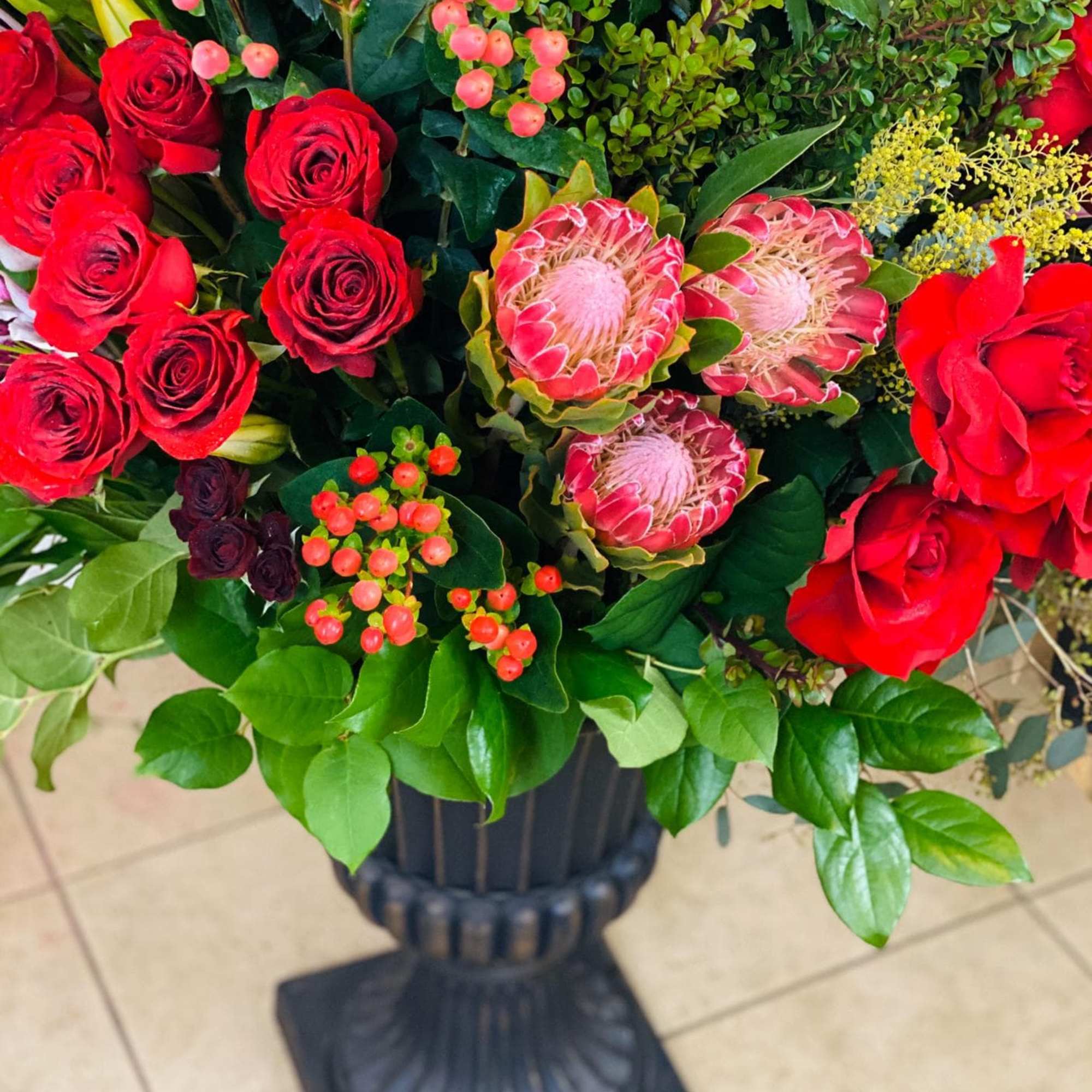 Red roses and pink protea in a black pedestal vase