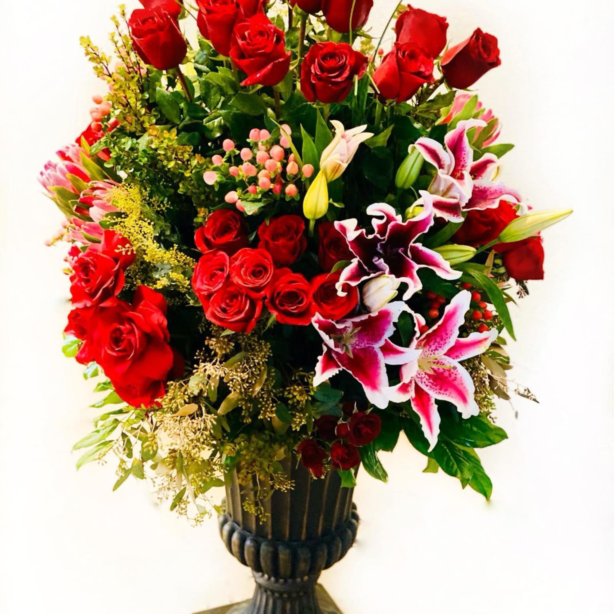 Tall arrangement of red roses and pink lilies in a dark pedestal vase