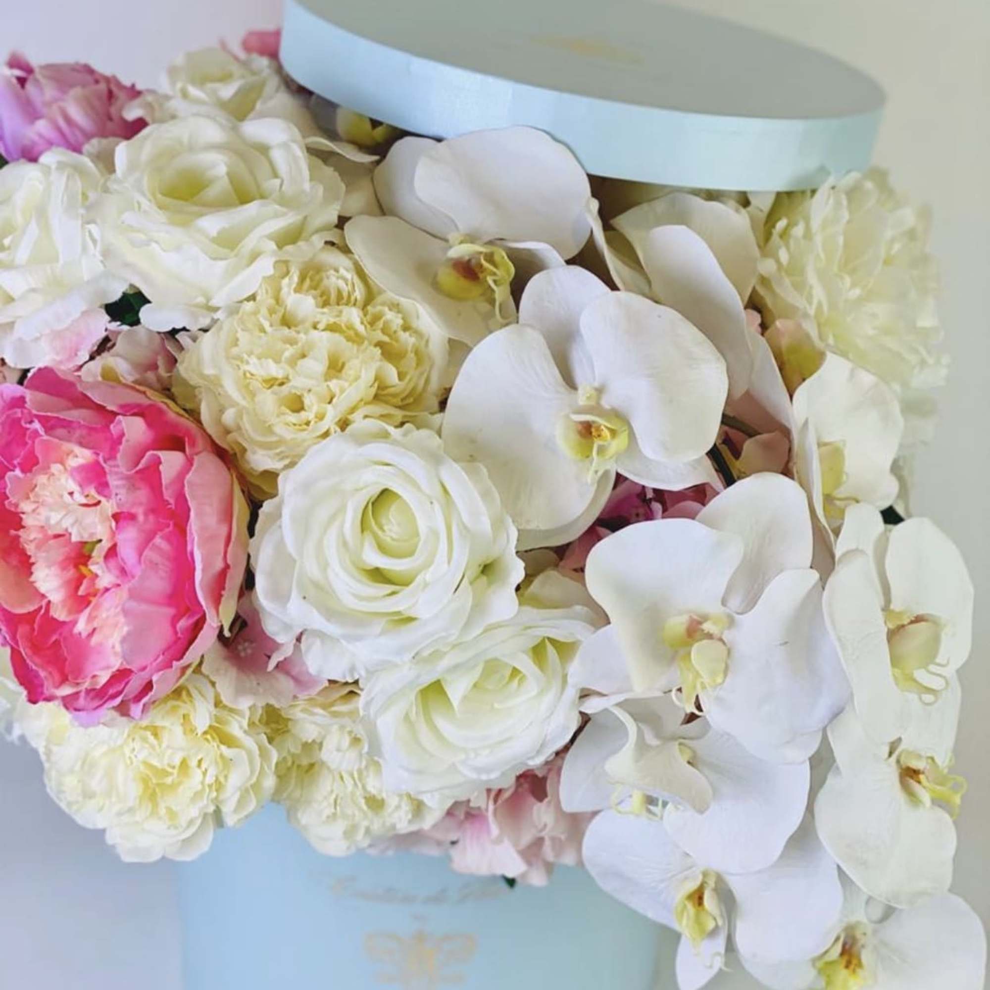 Pastel flower arrangement in a light blue hat box with white orchids and pink blooms