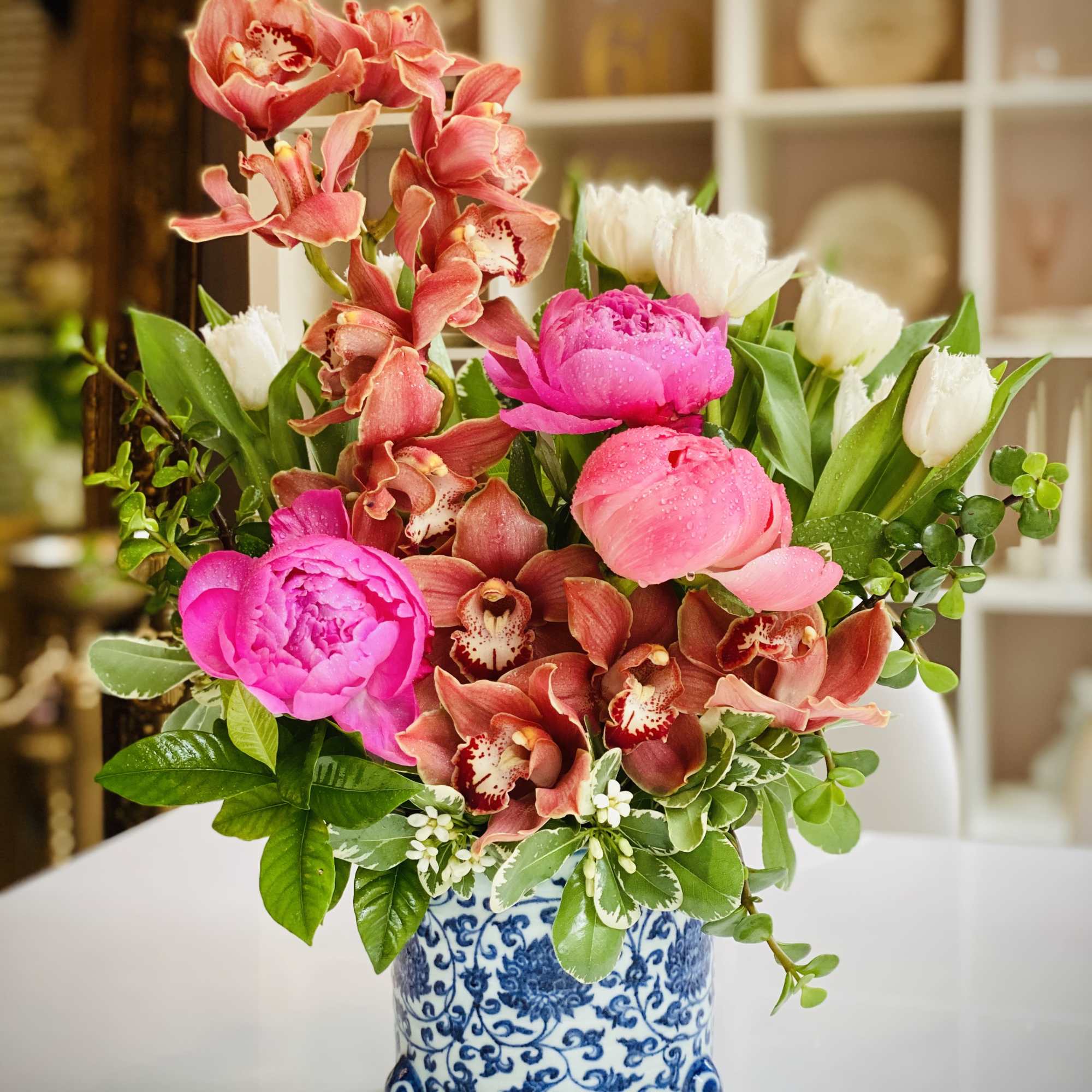 Pink peonies and orchids arranged in a blue-and-white ceramic vase