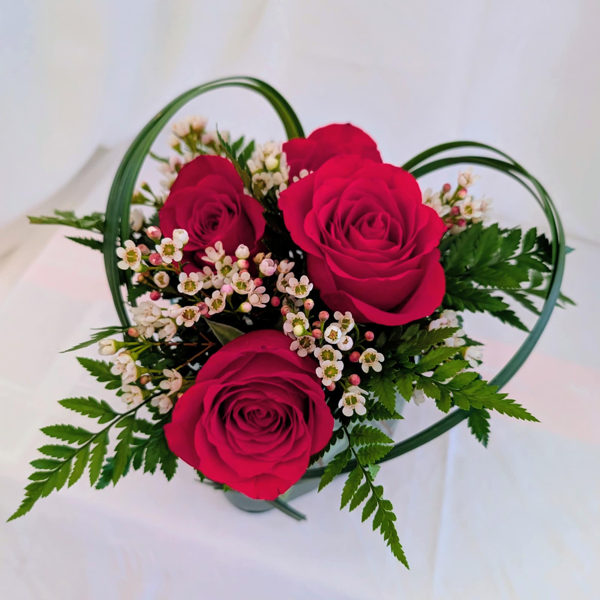 Pink roses arranged in a heart-shaped basket with small white filler flowers