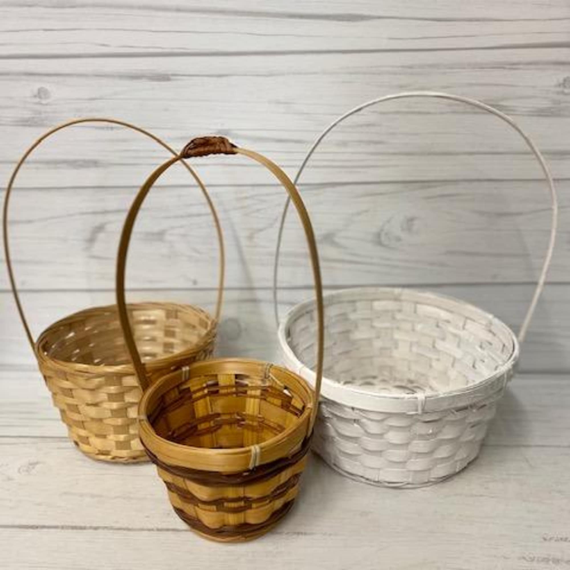 Three small woven baskets with wire handles on a light wood surface