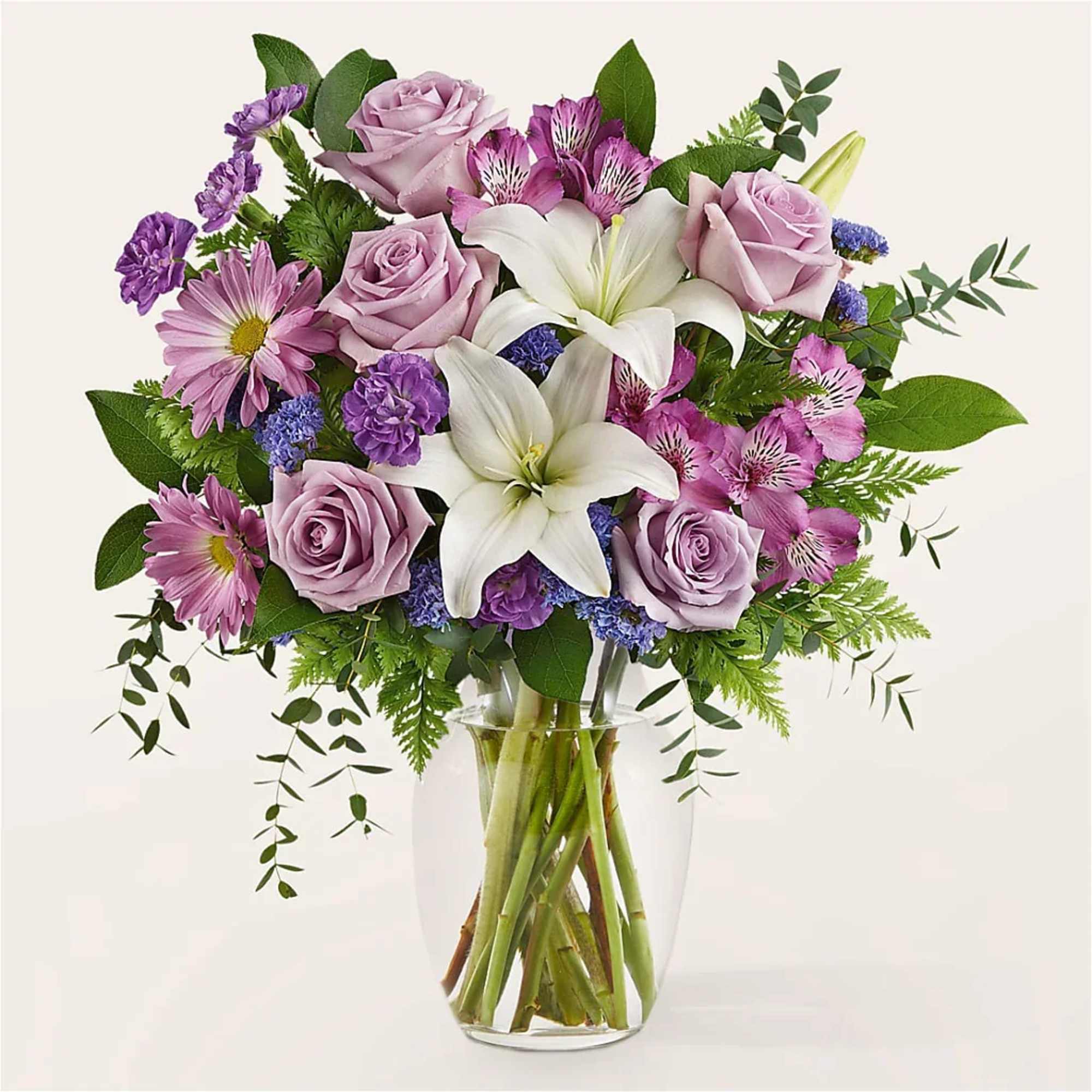 Mixed bouquet of lavender roses, white lilies and purple blooms in a clear glass vase