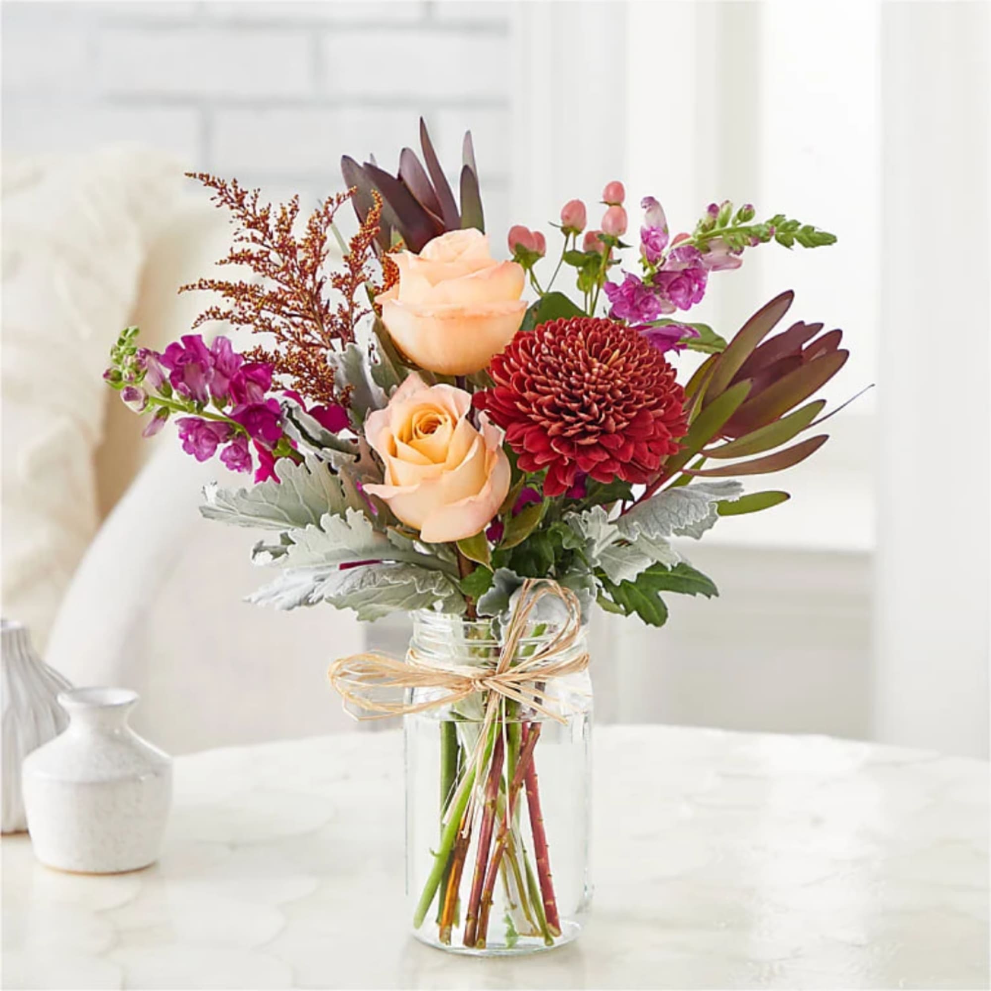 Peach roses and burgundy blooms in a clear glass jar vase
