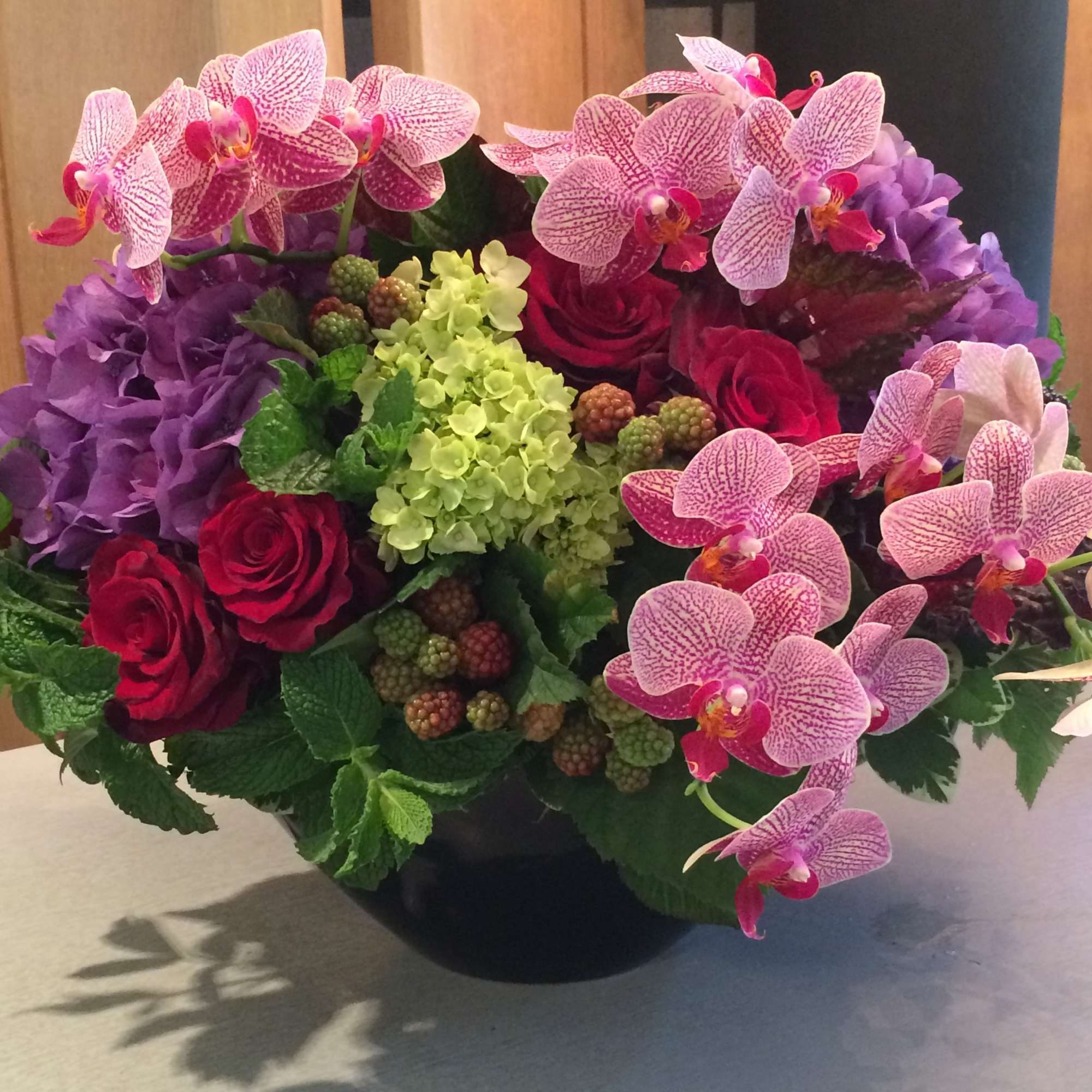 Bouquet of pink orchids, red roses, and purple hydrangeas in a black vase