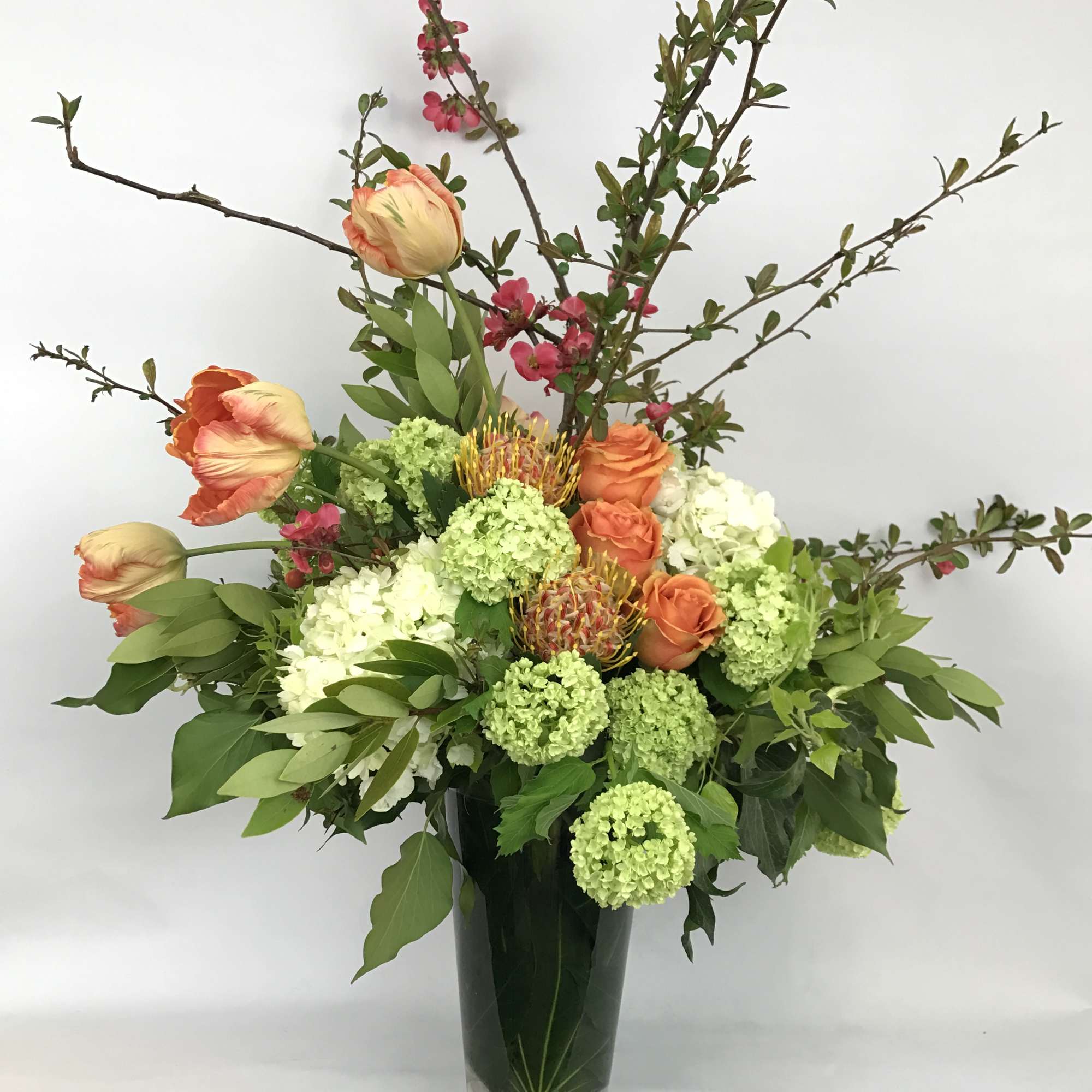 Tall floral arrangement with orange tulips, roses, and green hydrangeas in a glass vase