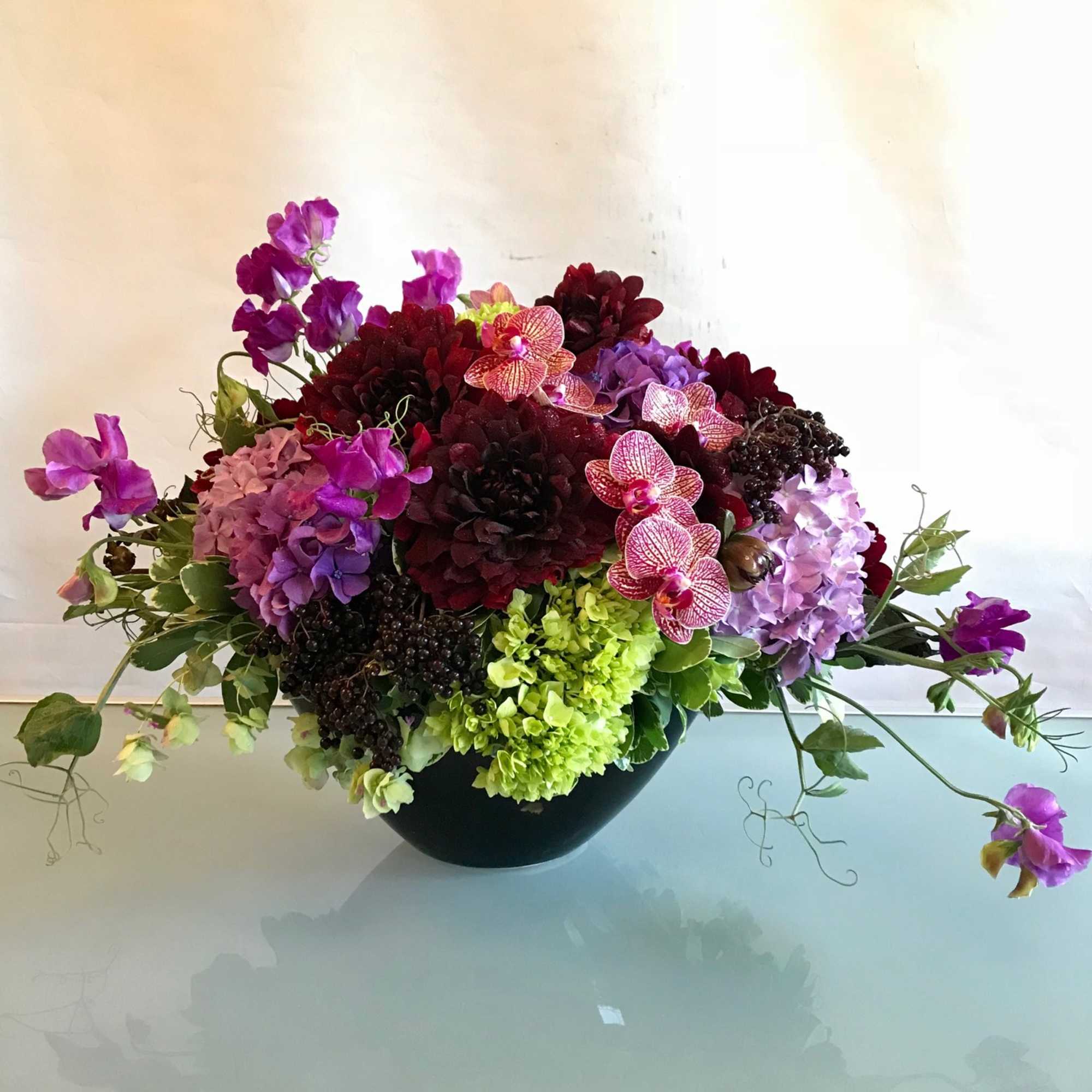 Colorful floral arrangement in a black bowl vase with orchids and hydrangeas