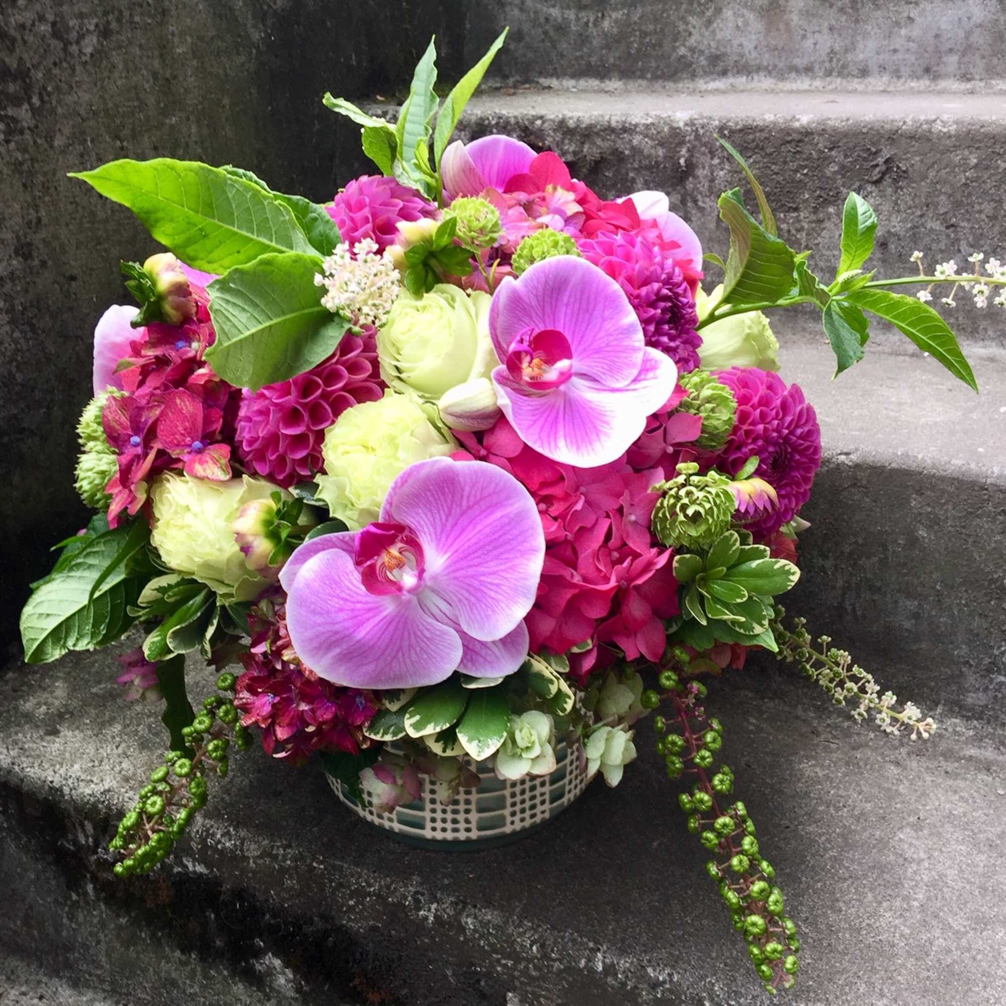 Pink and purple floral arrangement with orchids in a basket vase