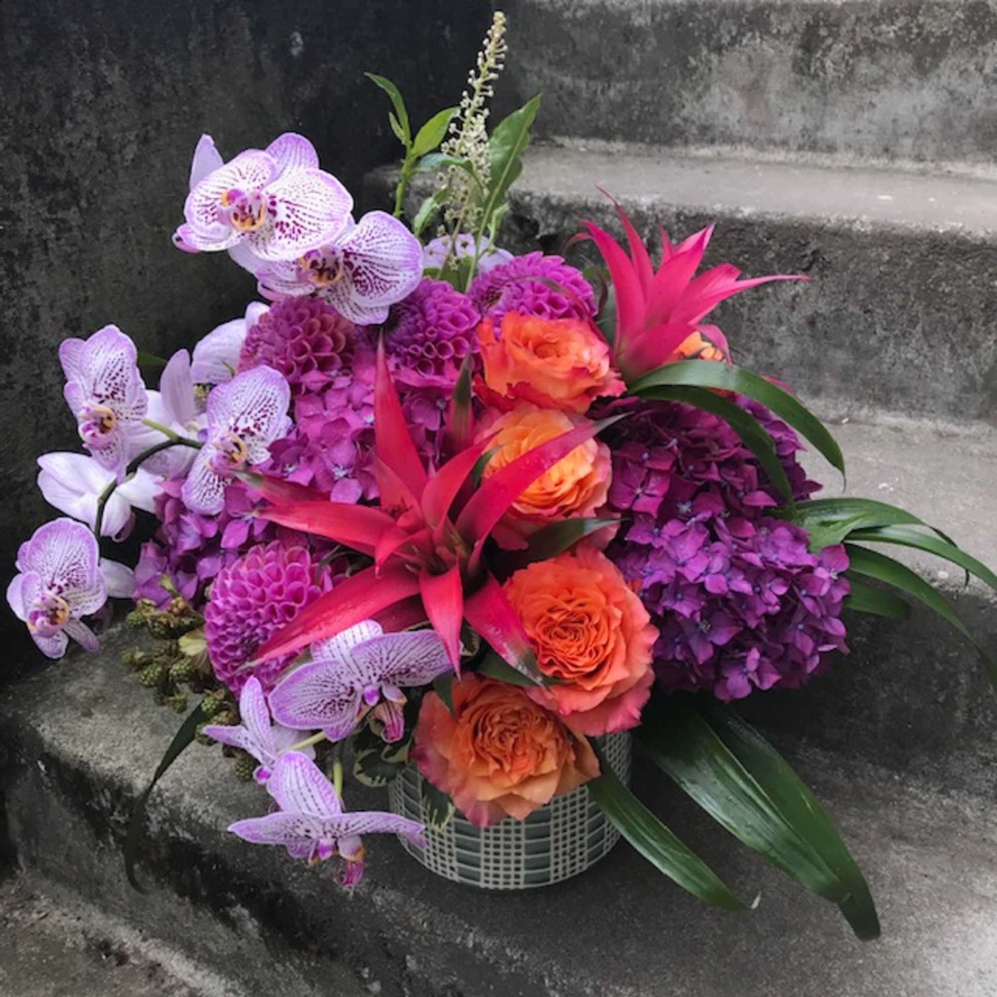 Tropical bouquet with orchids, orange roses, and purple blooms in a basket