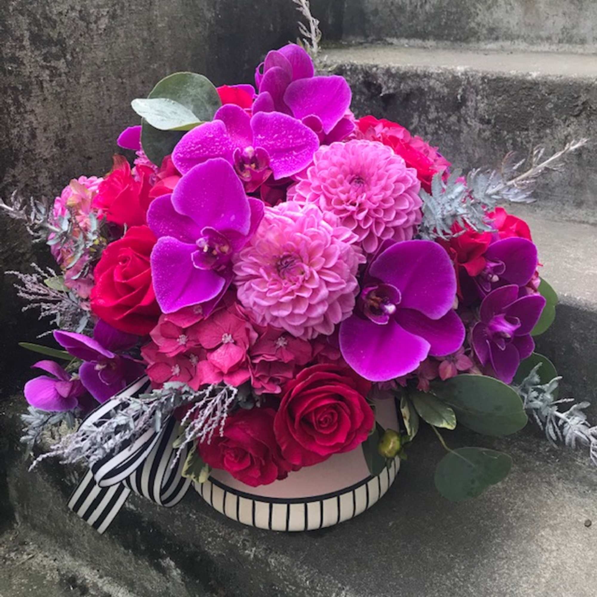 Pink and purple floral arrangement in a striped hatbox with ribbon
