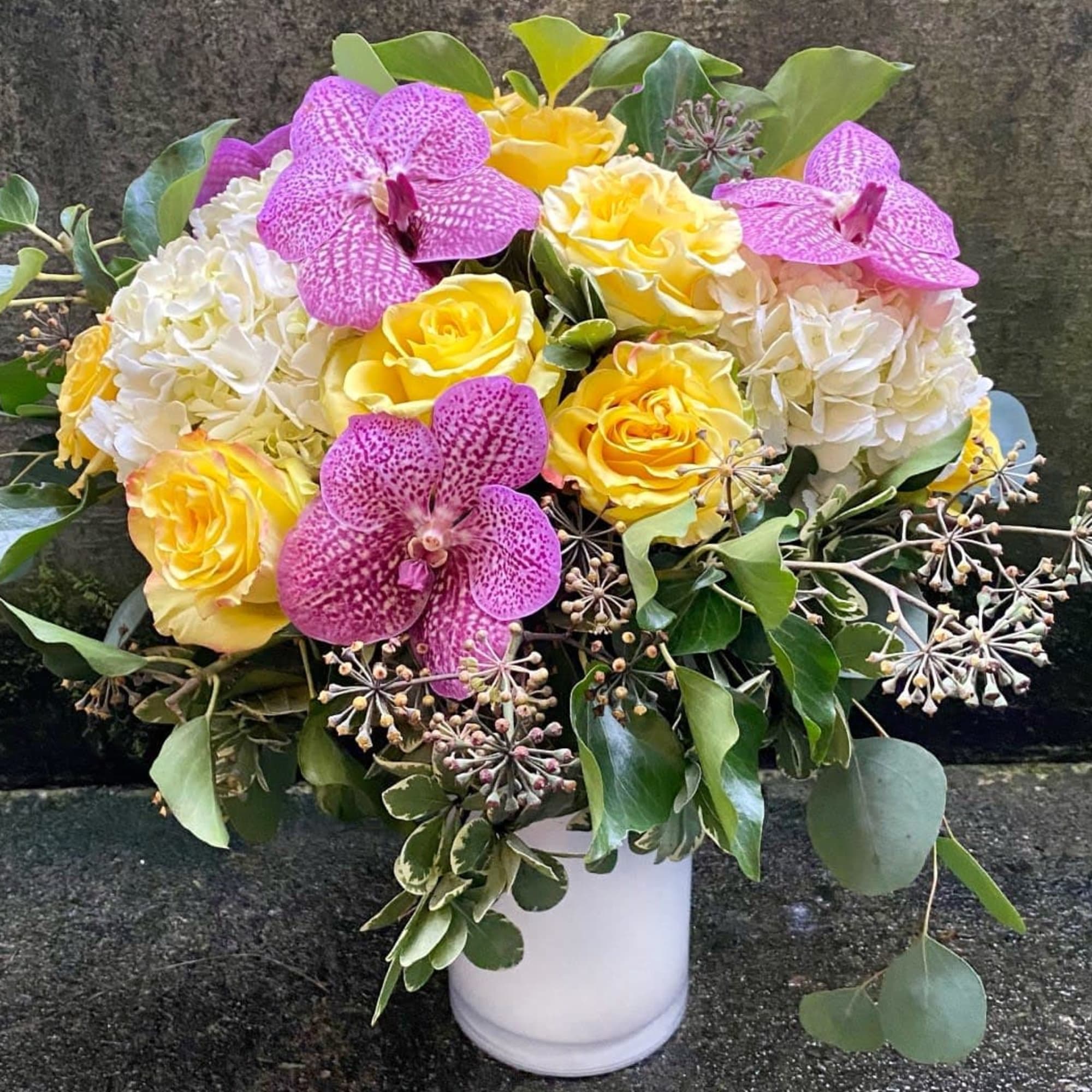 Bouquet of yellow roses, white hydrangeas, and pink orchids in a white vase