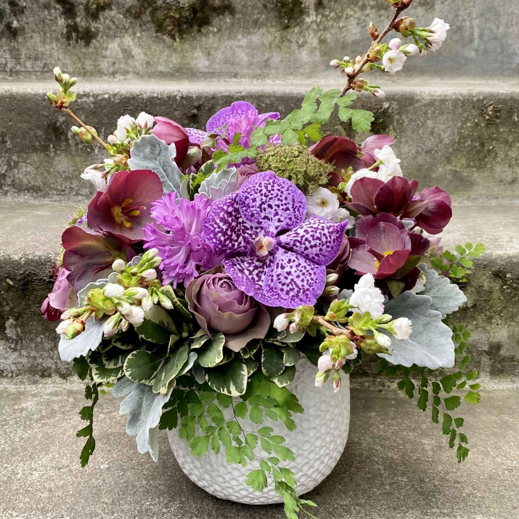Purple and burgundy floral arrangement in a white textured vase