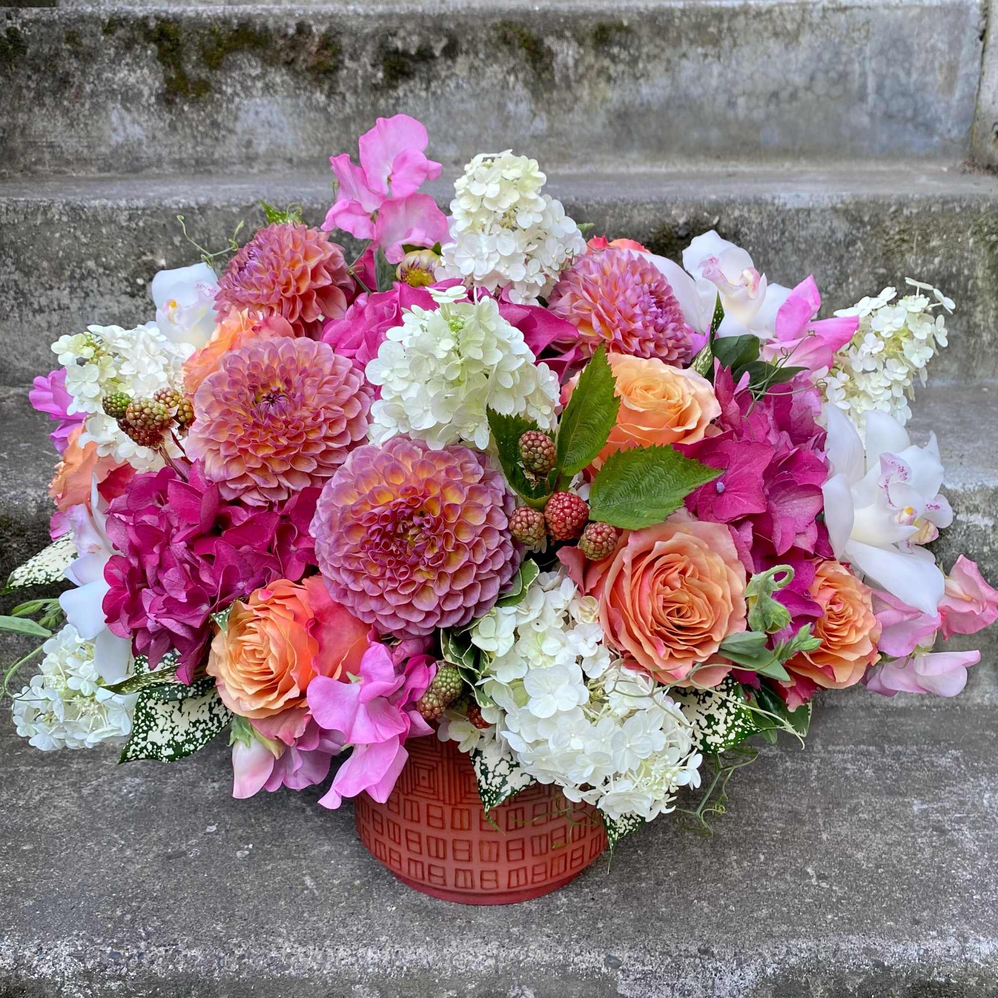 Pink and peach floral arrangement in a red container