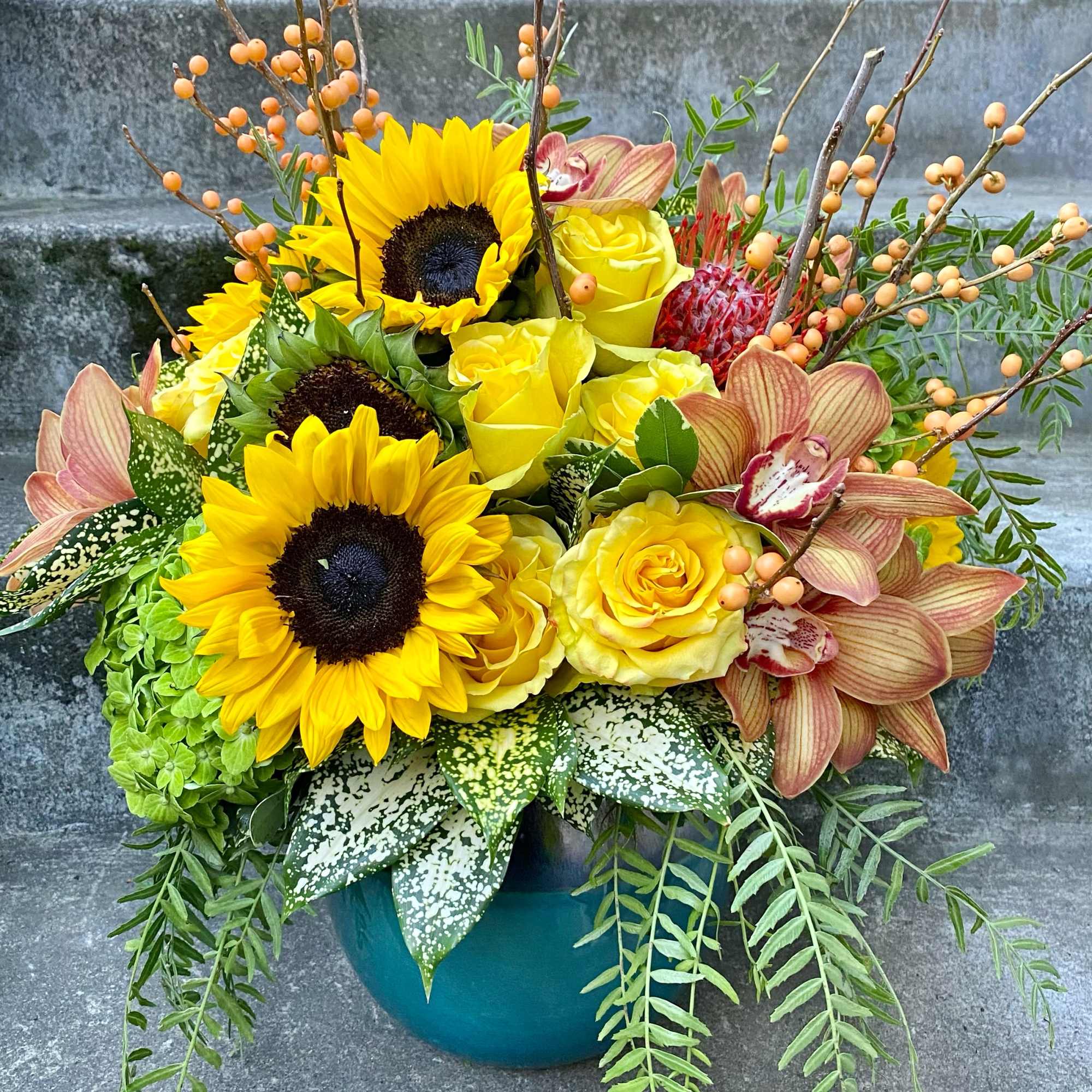 Bouquet of yellow sunflowers and roses in a teal vase