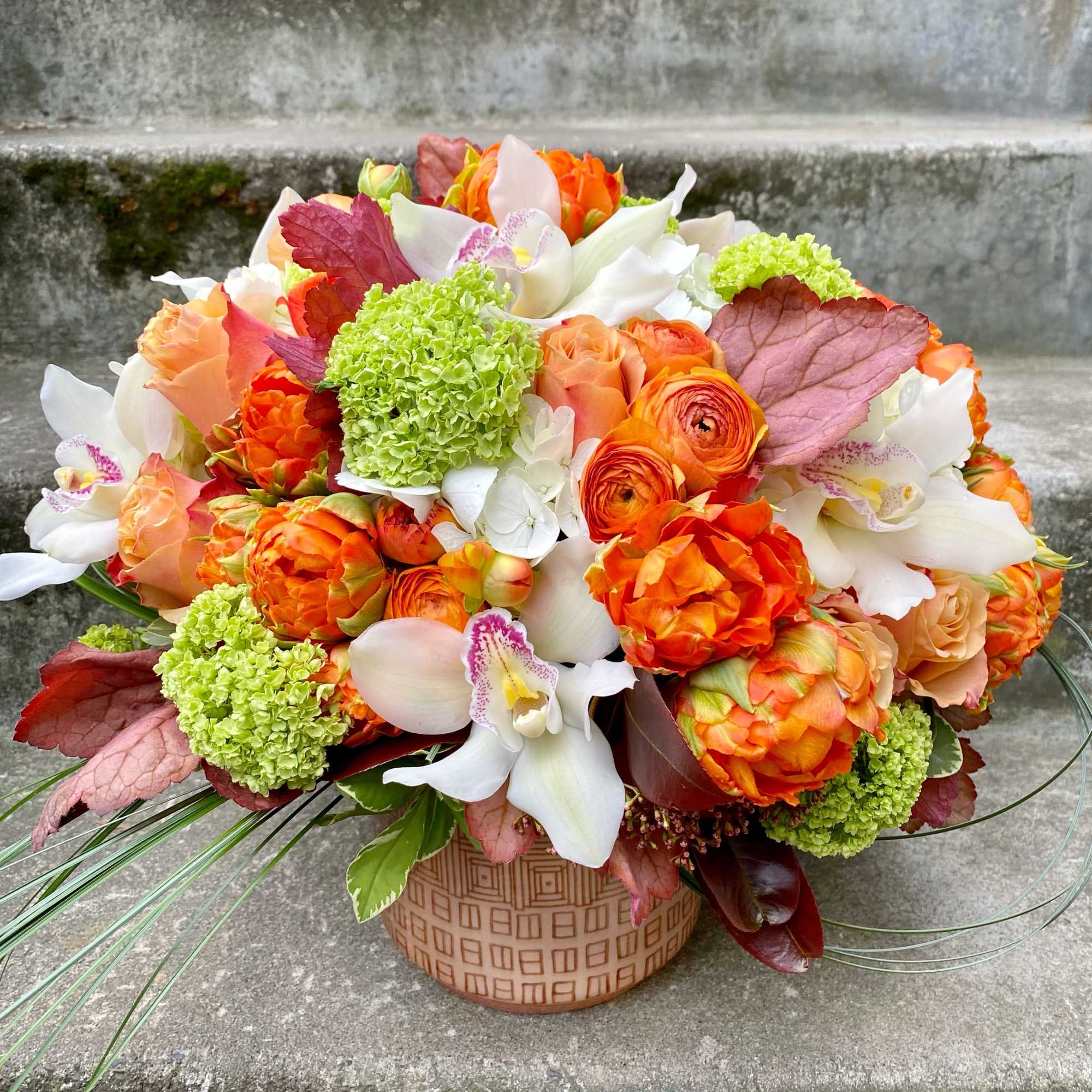 Orange and white floral arrangement in a patterned round vase