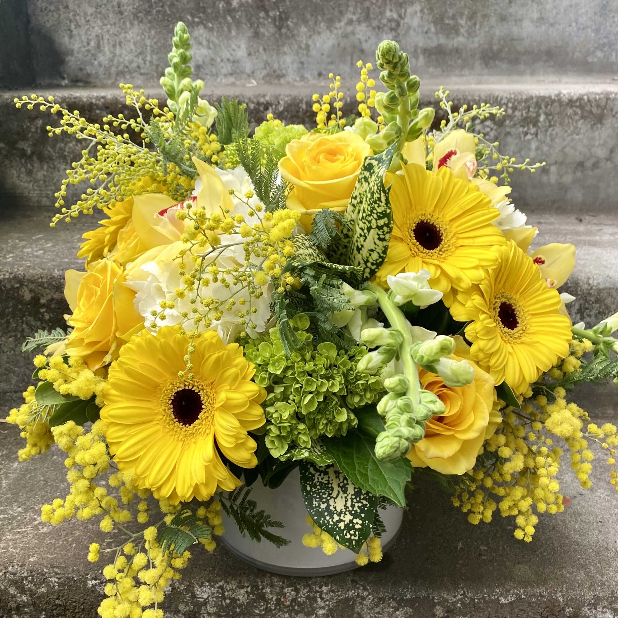 Yellow gerbera daisies and roses in a white container