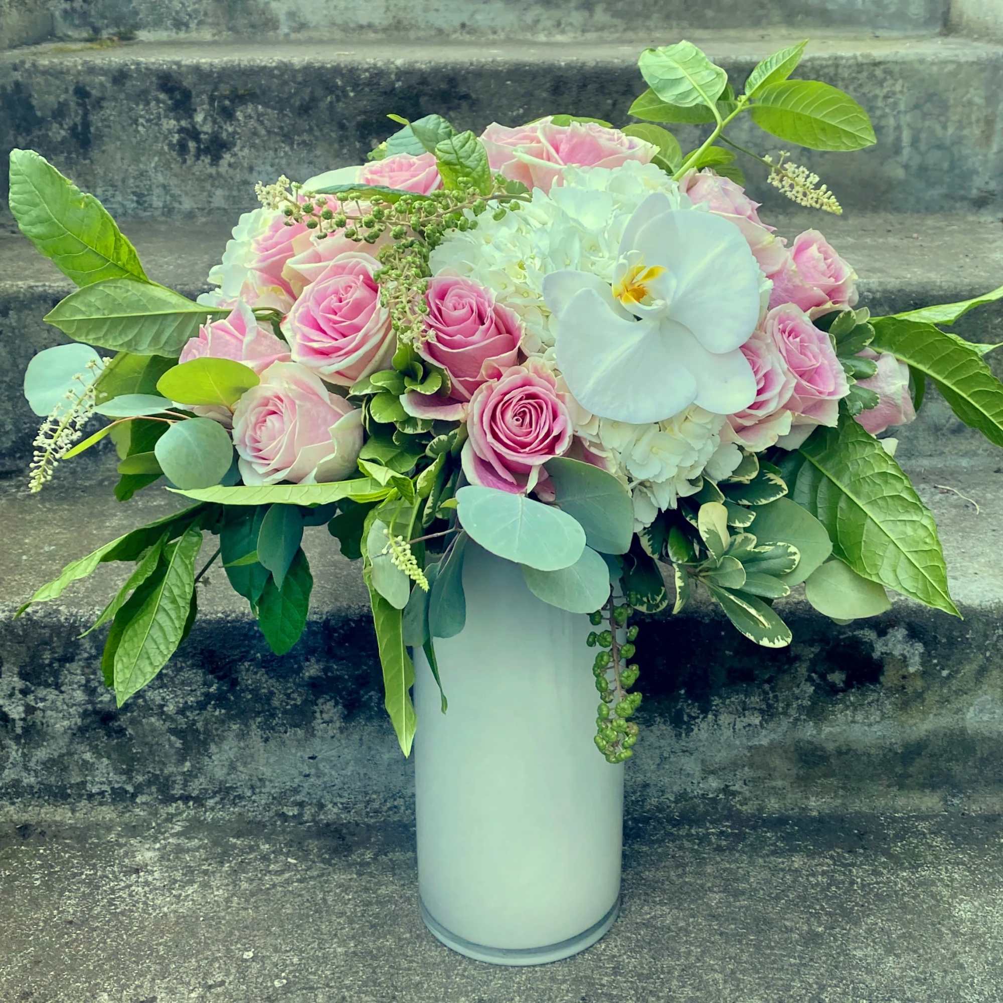 Pink roses and white orchids in a tall white vase