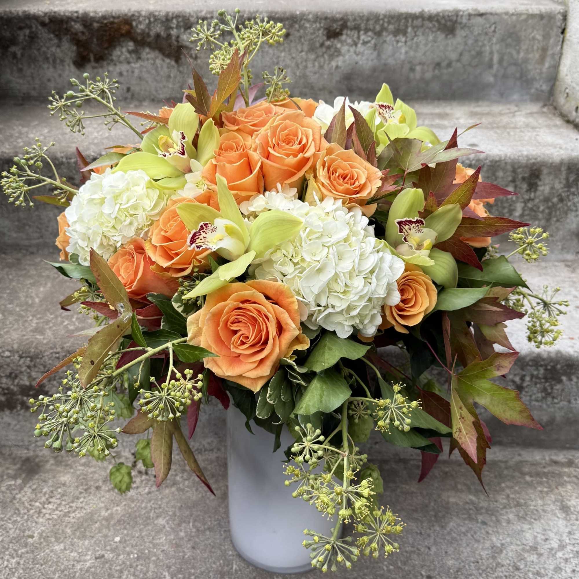 Orange roses and white hydrangeas in a white vase with green orchids