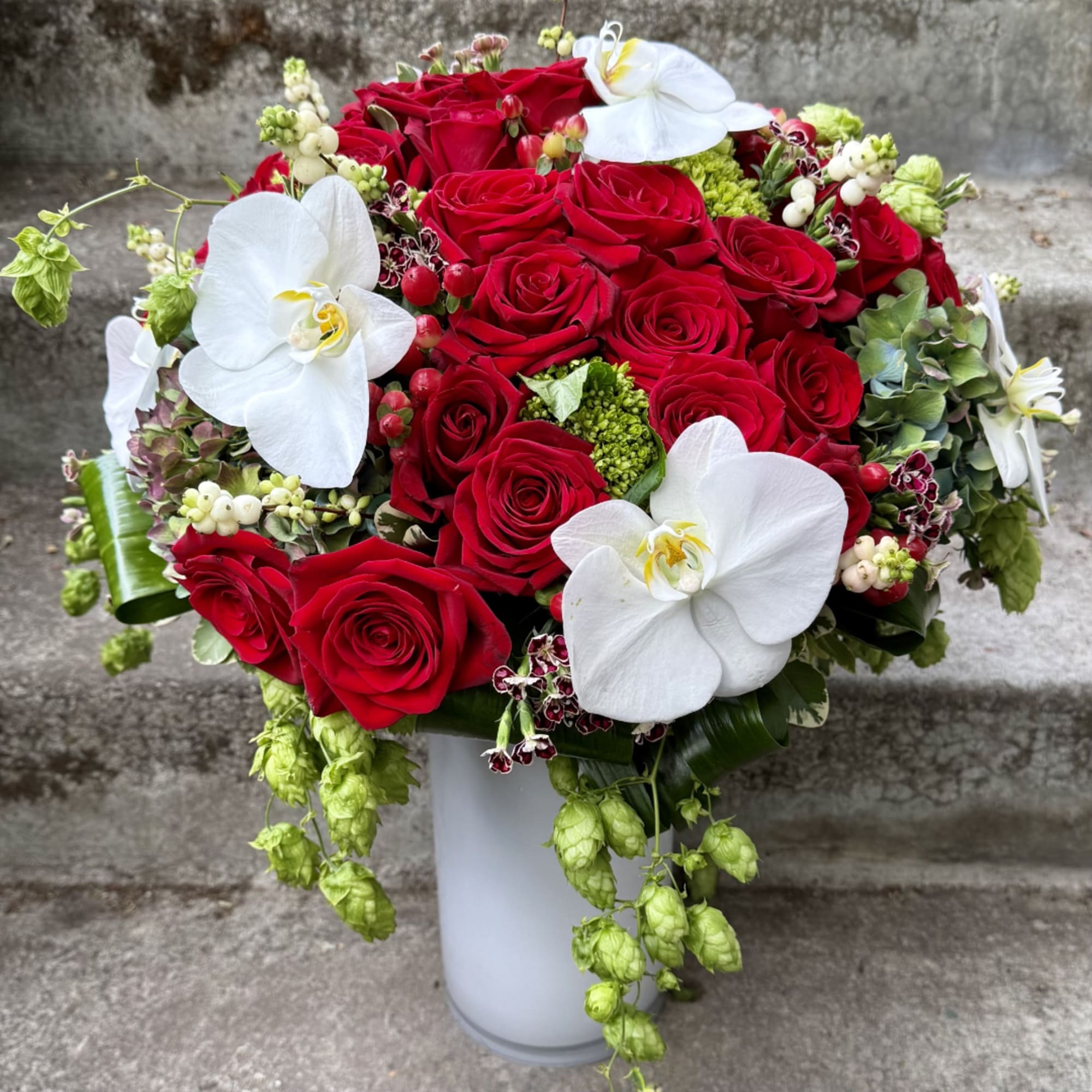 Red roses and white orchids arranged in a white vase