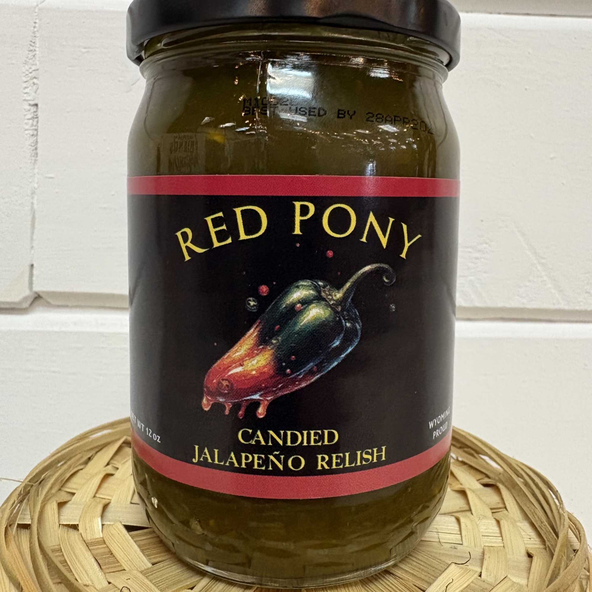 Jar of candied jalapeño relish with a black lid on a woven tray