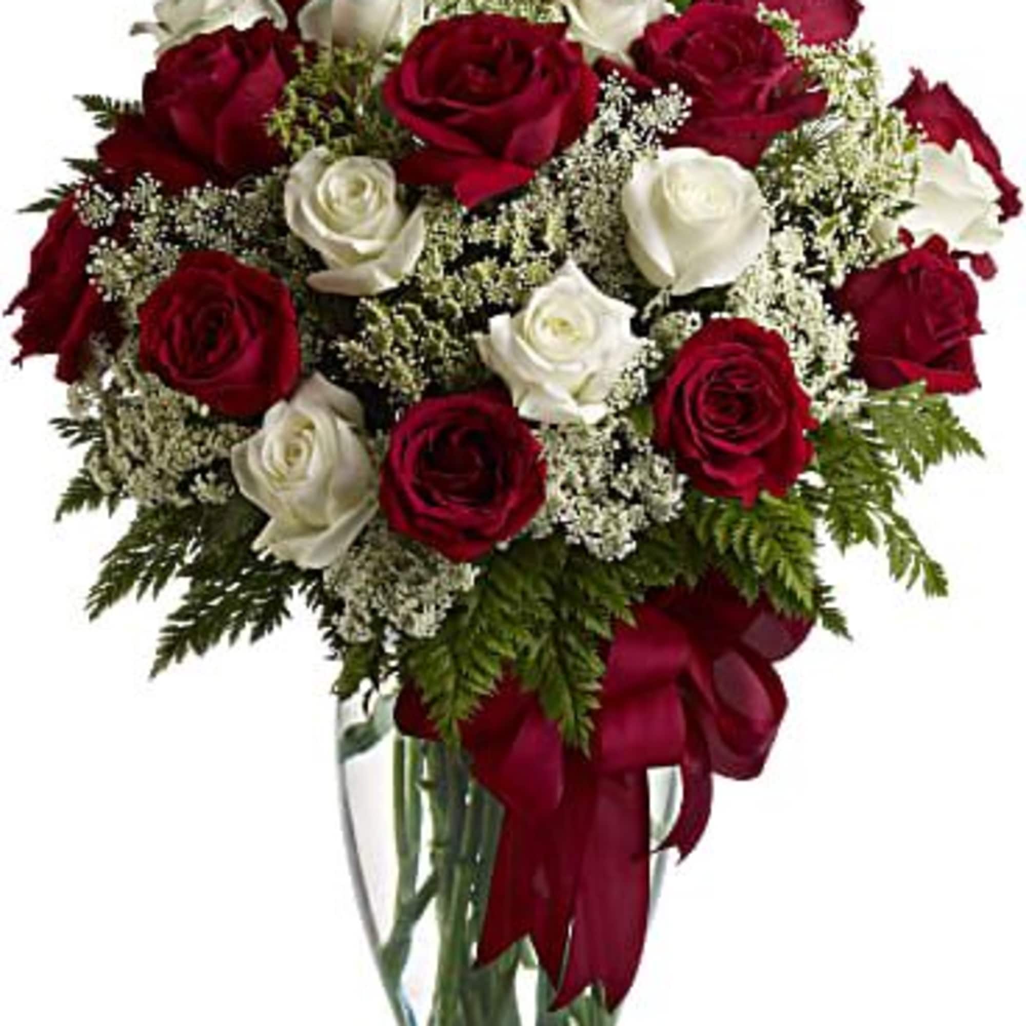 Arrangement of red and white roses in a clear glass vase with a red ribbon bow.
