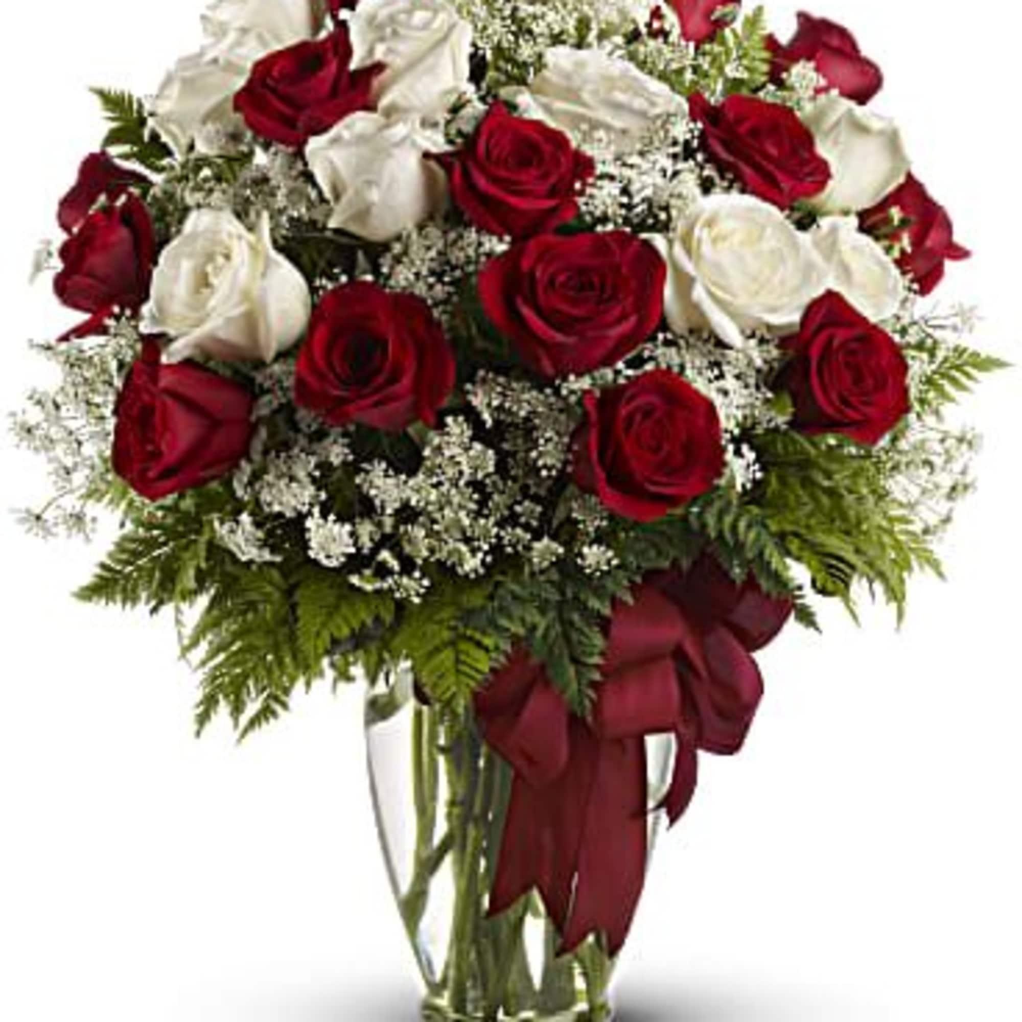 Arrangement of red and white roses with white filler flowers in a clear glass vase with a red ribbon.