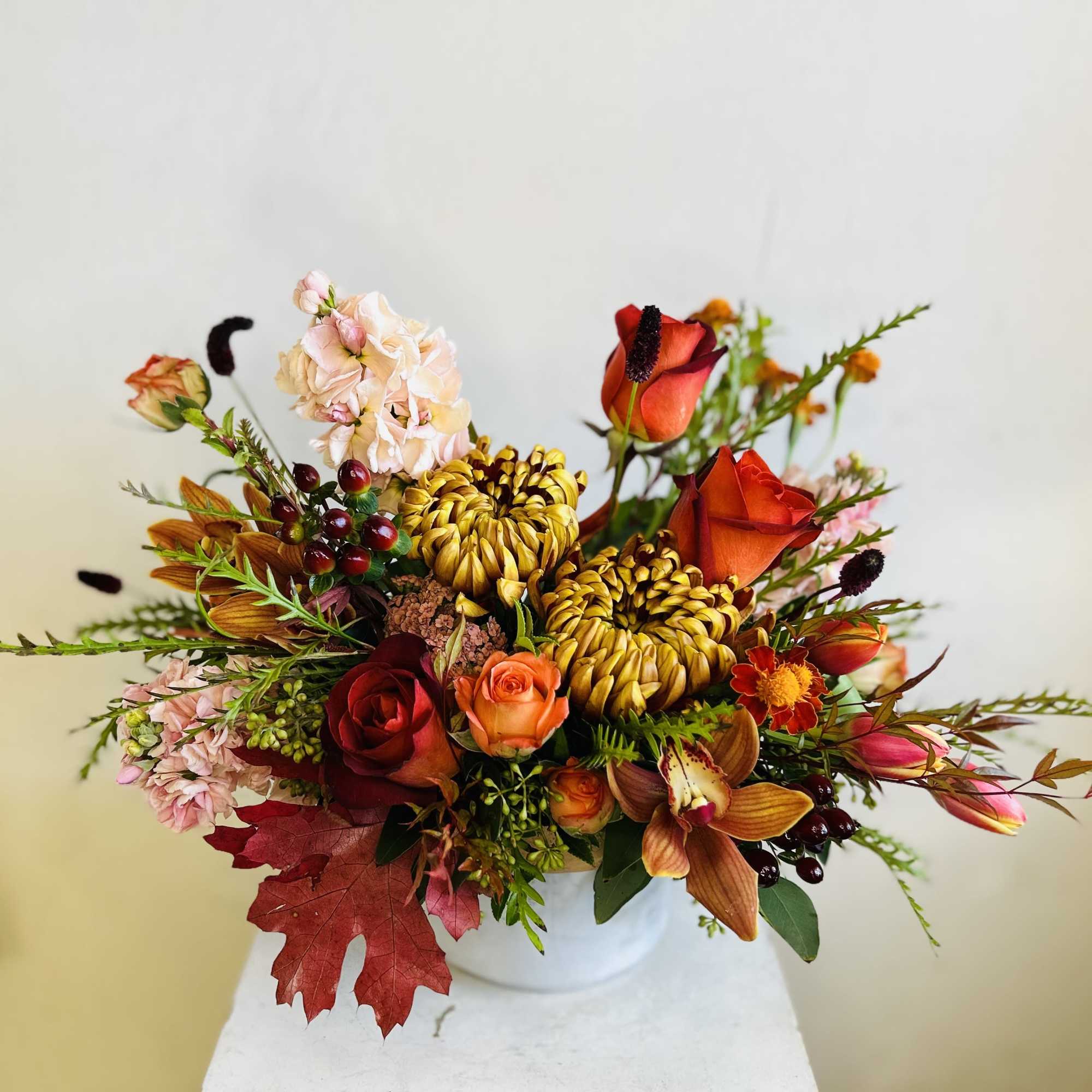 Mixed bouquet of orange, red, and blush flowers in a white vase