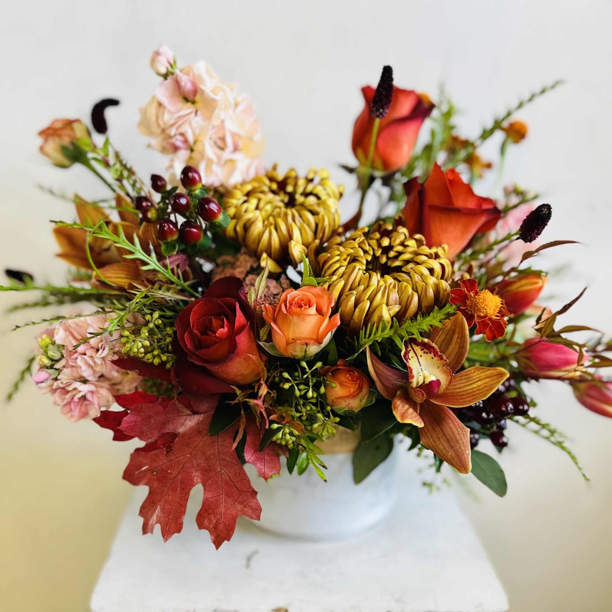 Autumn bouquet of roses, orchids, and mums in a white vase